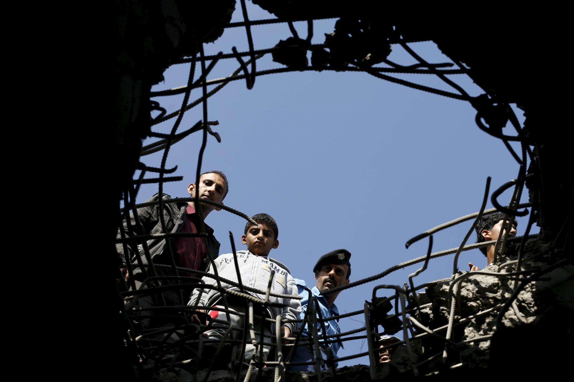 People look through a hole caused by a Saudi-led air strike