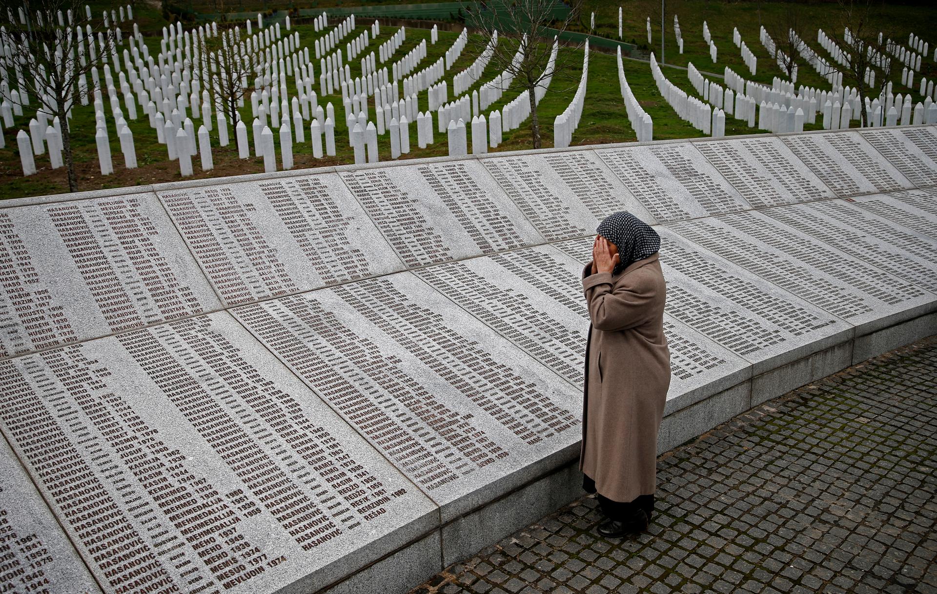 A woman prays near a war crimes memorial.
