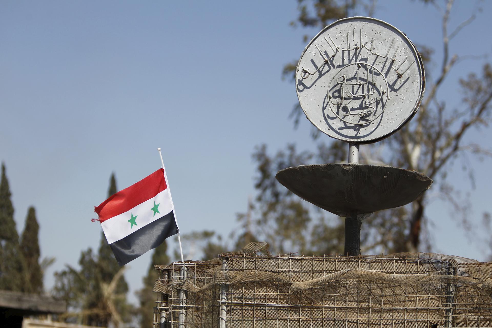 A Syrian national flag flutters next to the Islamic State's slogan at a roundabout where executions were carried out by ISIS militants in the city of Palmyra, in Homs Governorate, Syria April 1, 2016.