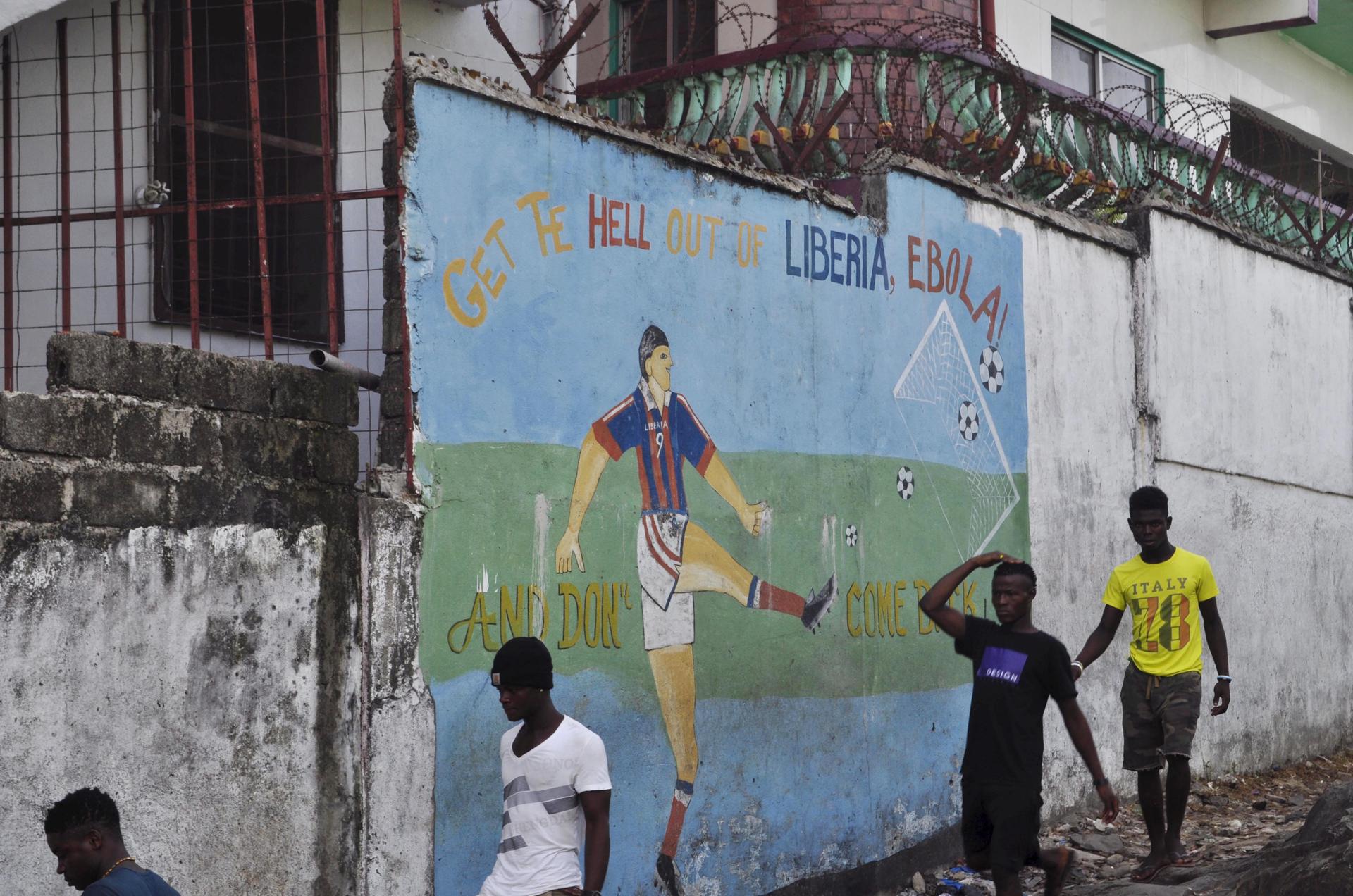 Men walk by a mural that reads "Get the hell of Liberia, Ebola! And don't come back" in Monrovia, Liberia, April 1, 2016.