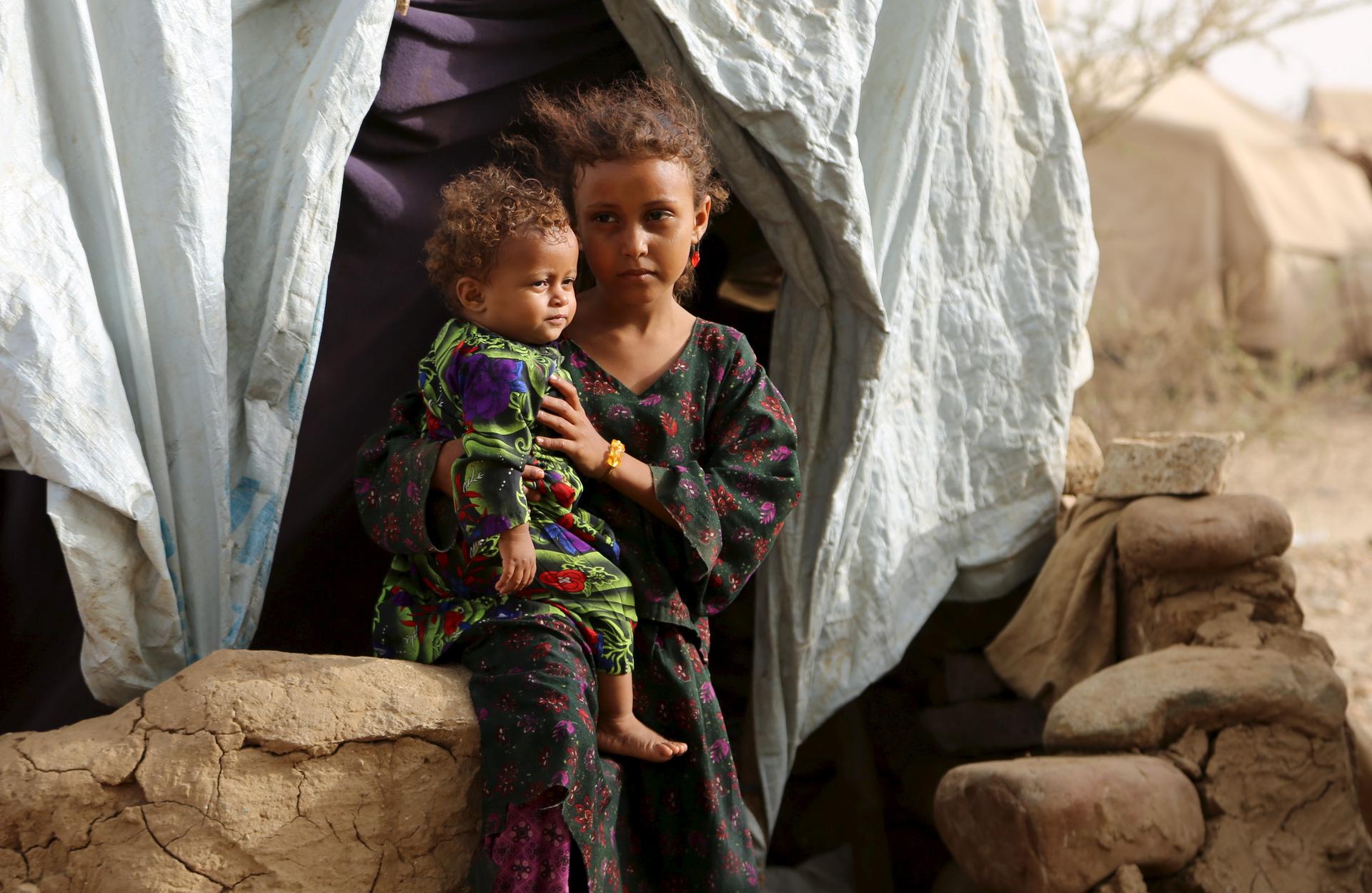 A girl holds her sister outside their family's hut at the Shawqaba camp for internally displaced people who were forced to leave their villages by the war in Yemen's northwestern province of Hajjah March 12, 2016
