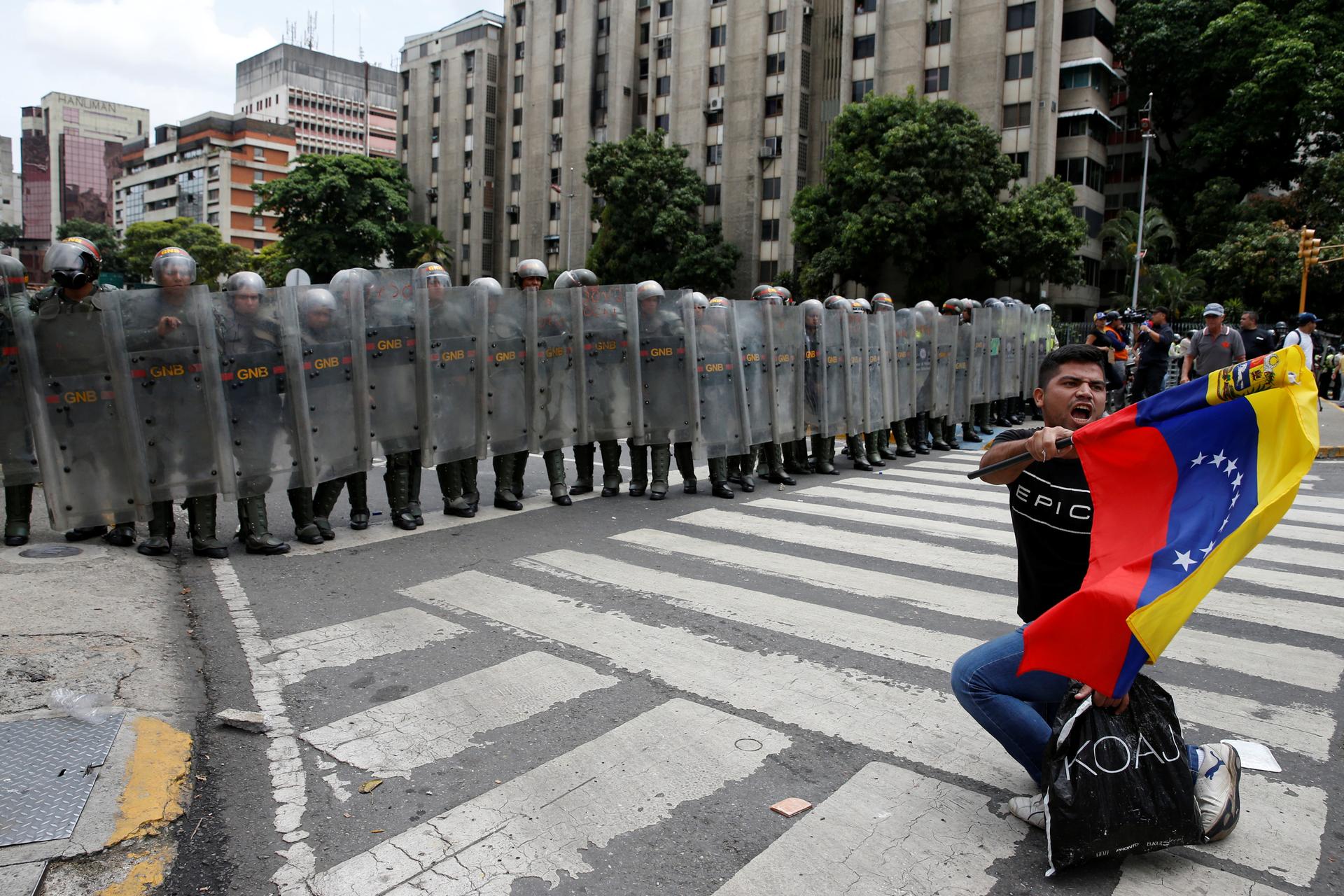 An opposition supporter carrying a Venezuelan flag kneels in front of National Guards during a rally to demand a referendum to remove President Nicolas Maduro in Caracas, Venezuela, May 18, 2016.