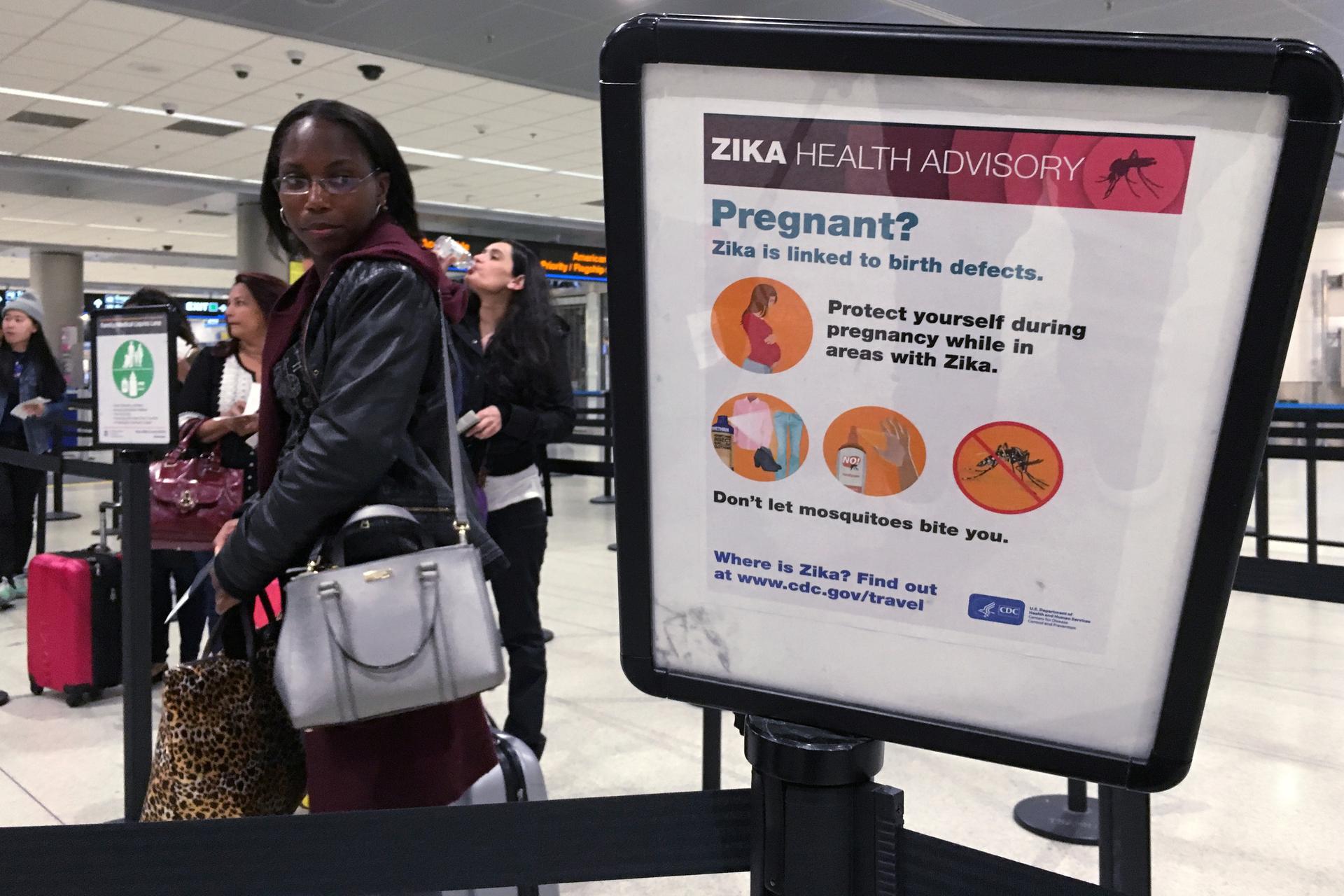 A woman looks at a Center for Disease Control (CDC) health advisory sign about the dangers of the Zika virus as she lines up for a security screening at Miami International Airport in Miami, Florida, U.S., May 23, 2016. 