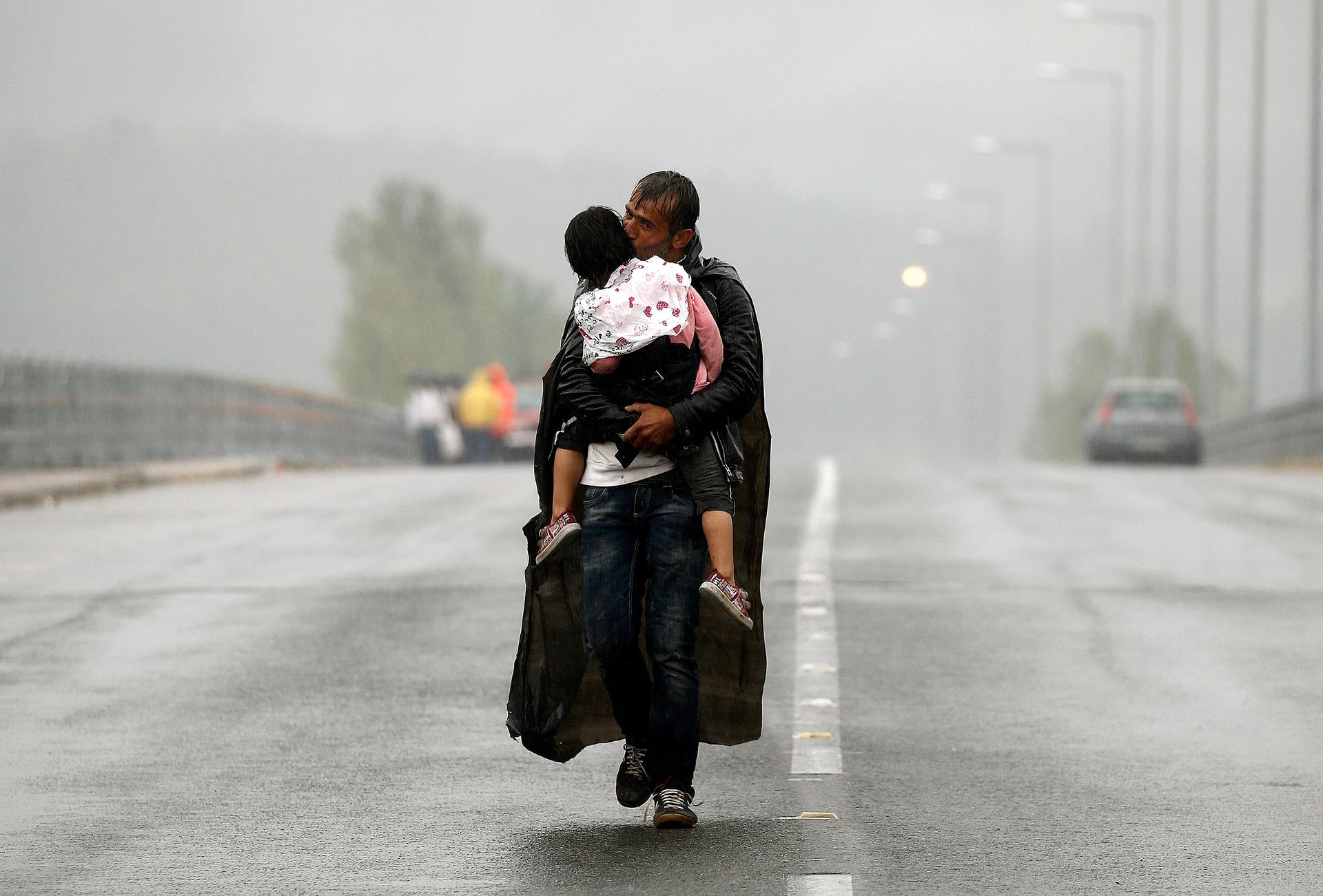 A Syrian refugee kisses his son as he walks through a rainstorm towards Greece's border with Macedonia.