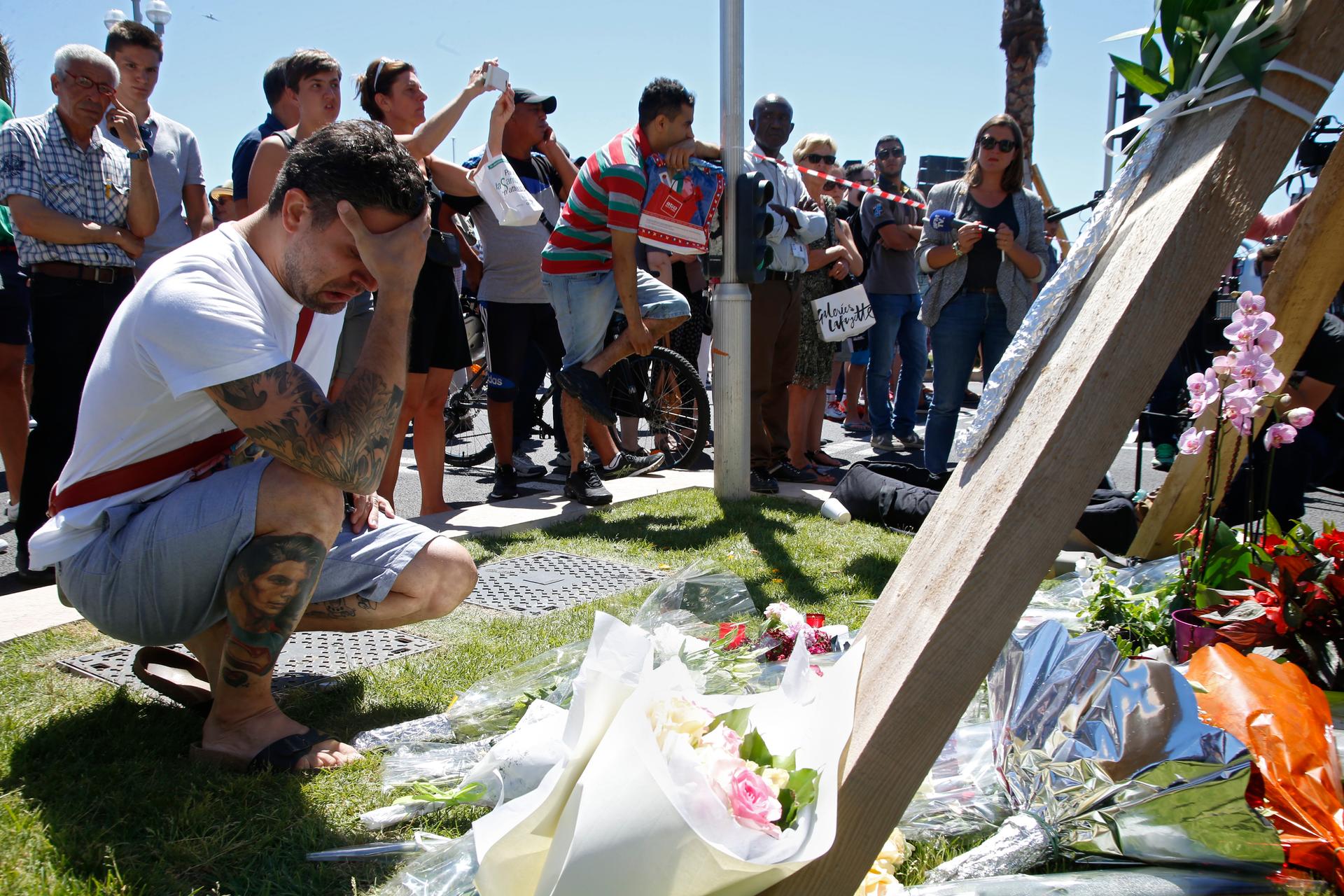 Man kneels in front of make-shift memorial with head in hands