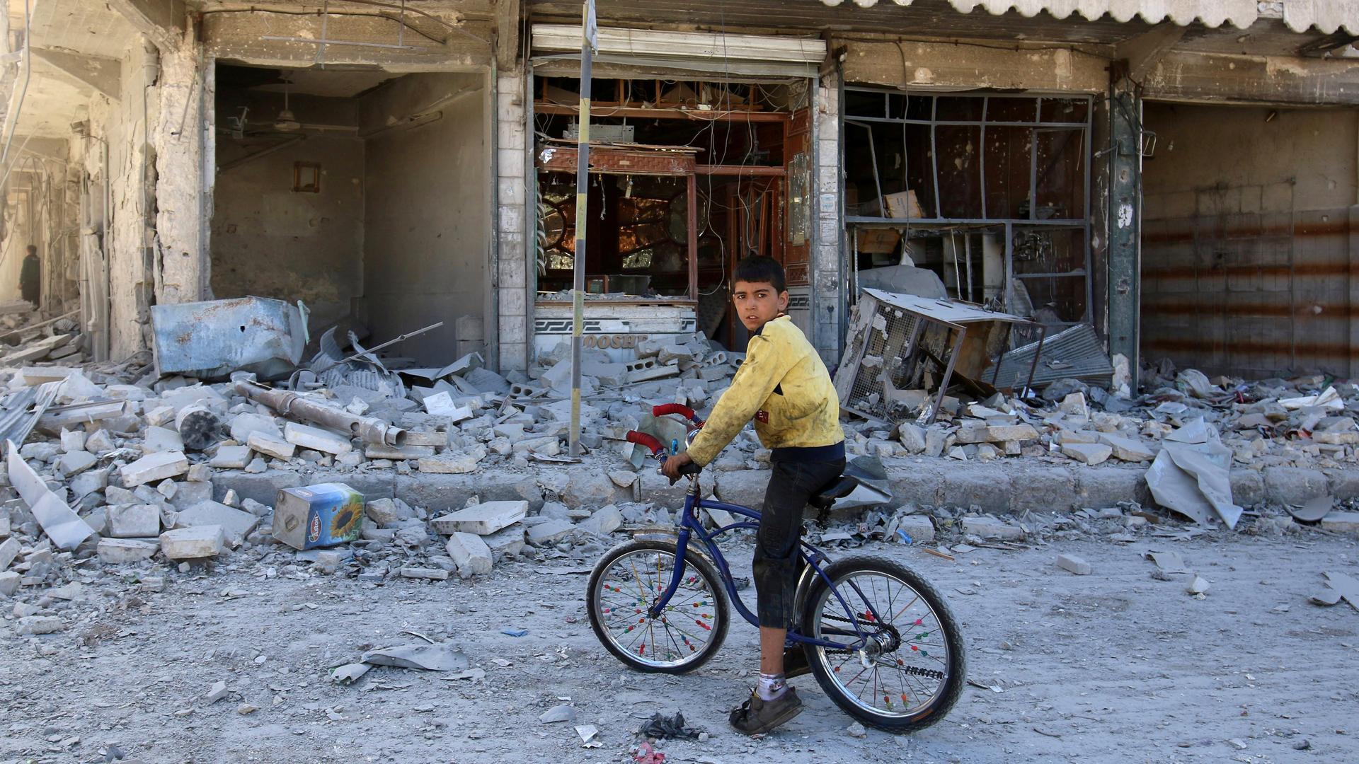 A boy sits on a bicycle in front of damaged shops after an airstrike on the rebel held al-Qaterji neighborhood of Aleppo, Syria.