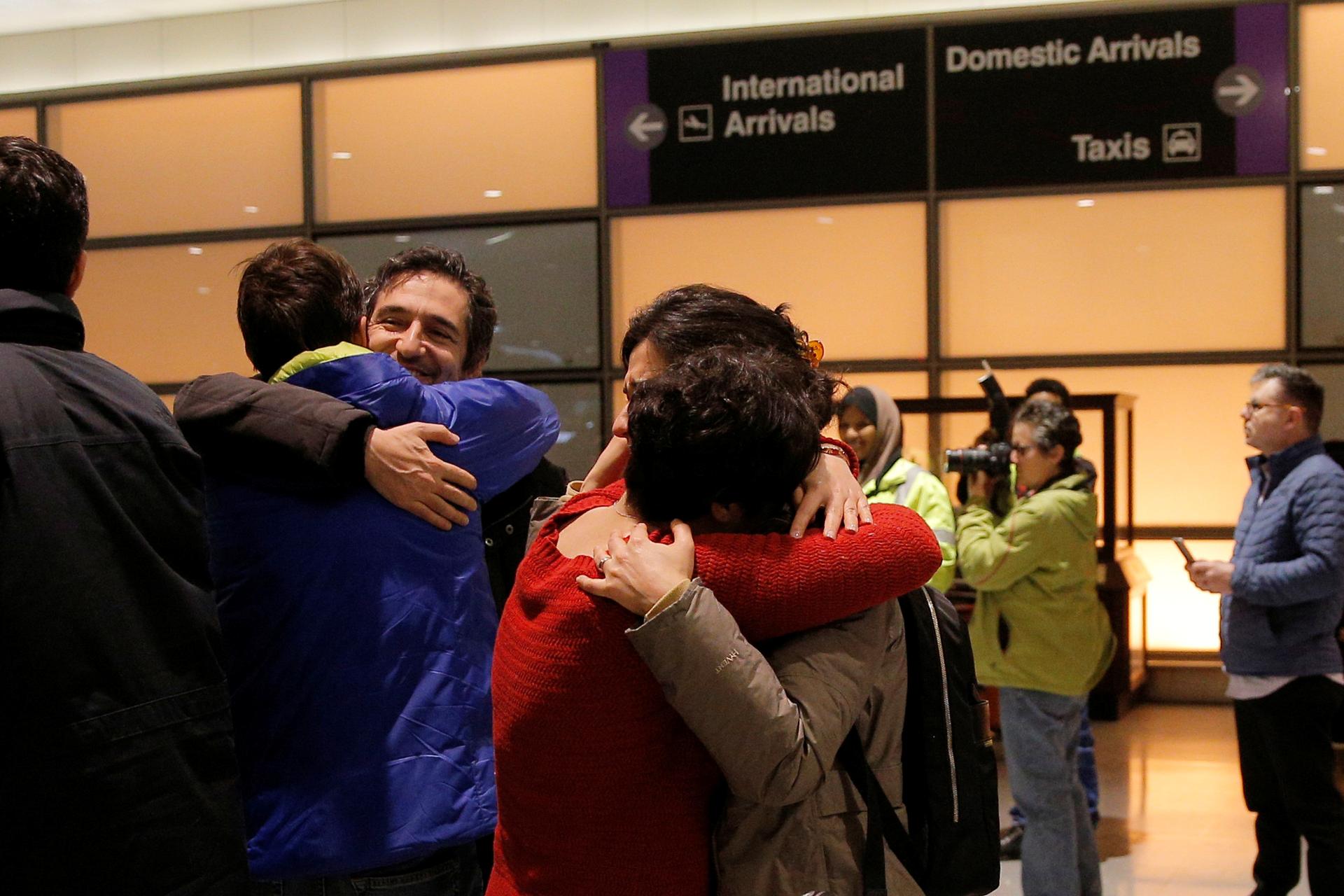 People hugging in front of airport arrival and departure signs