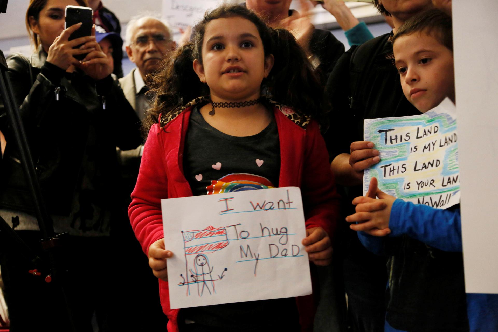 Young girl holding sign in front of crowd, "I want to hug my dad"