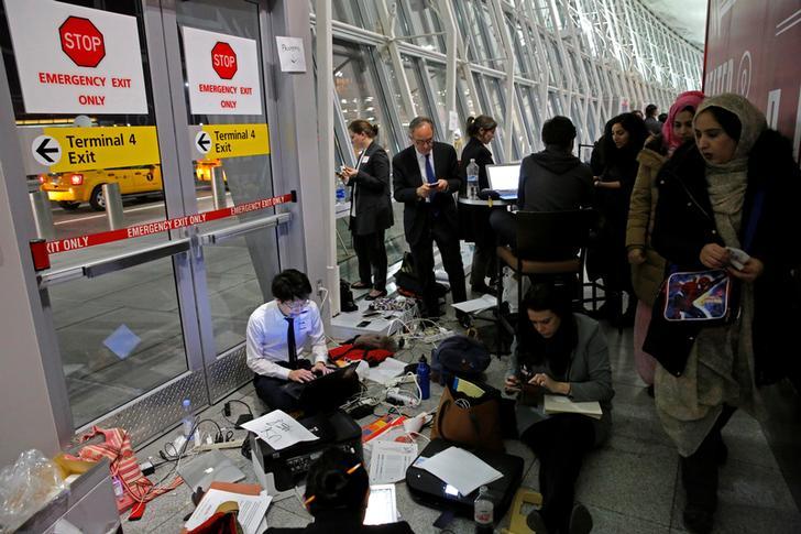 ​Women walk by a team of volunteer lawyers in their makeshift office working to assist travelers detained as part of Donald Trump's travel ban in Terminal 4 at John F. Kennedy International Airport in Queens.