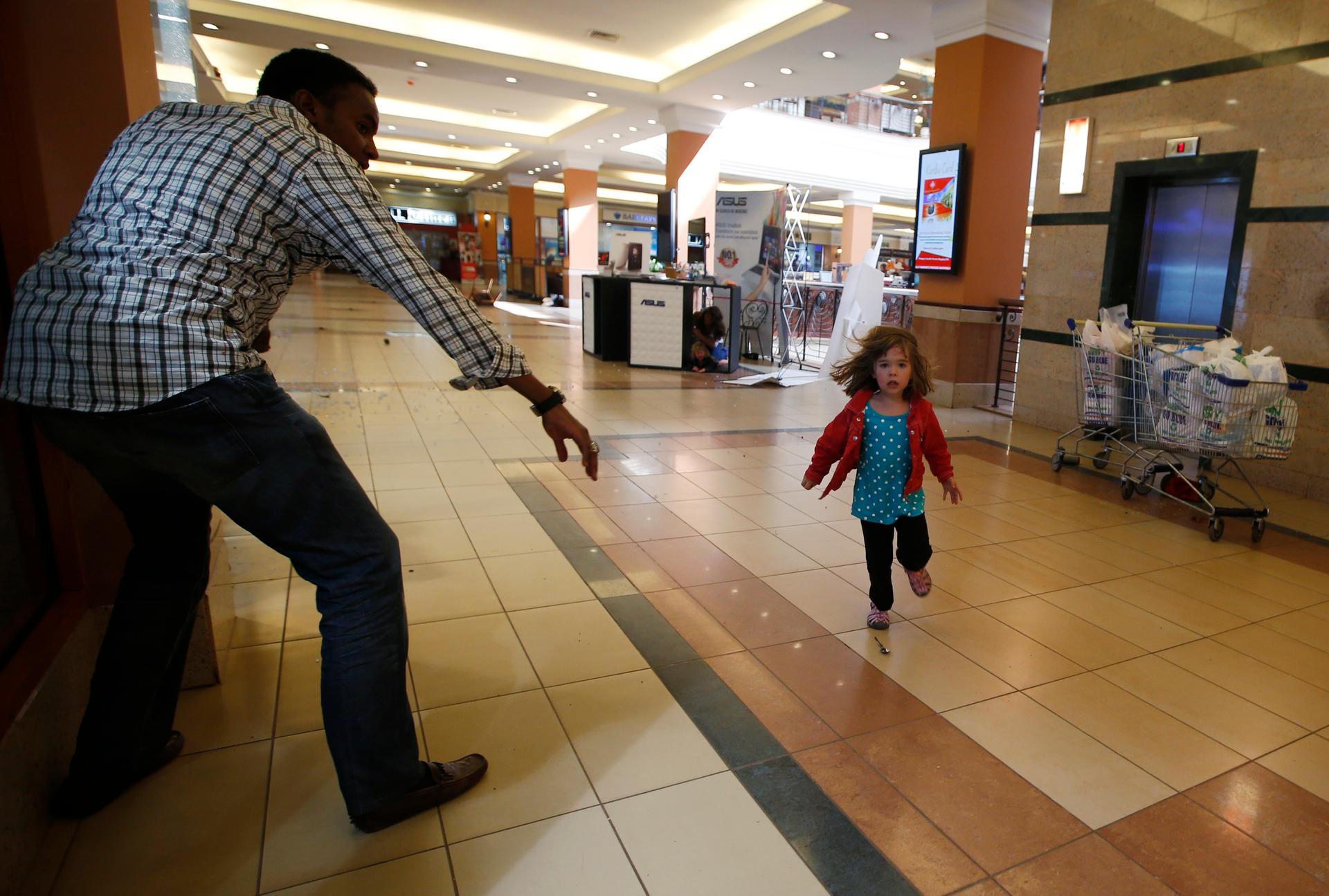 Four year old Portia Walton runs toward Abdul Haji during the Westgate Mall massacre. Her mom and others shelter under the black and white table in the middle. The terrorists are holed up and firing from the supermarket beyond the table.