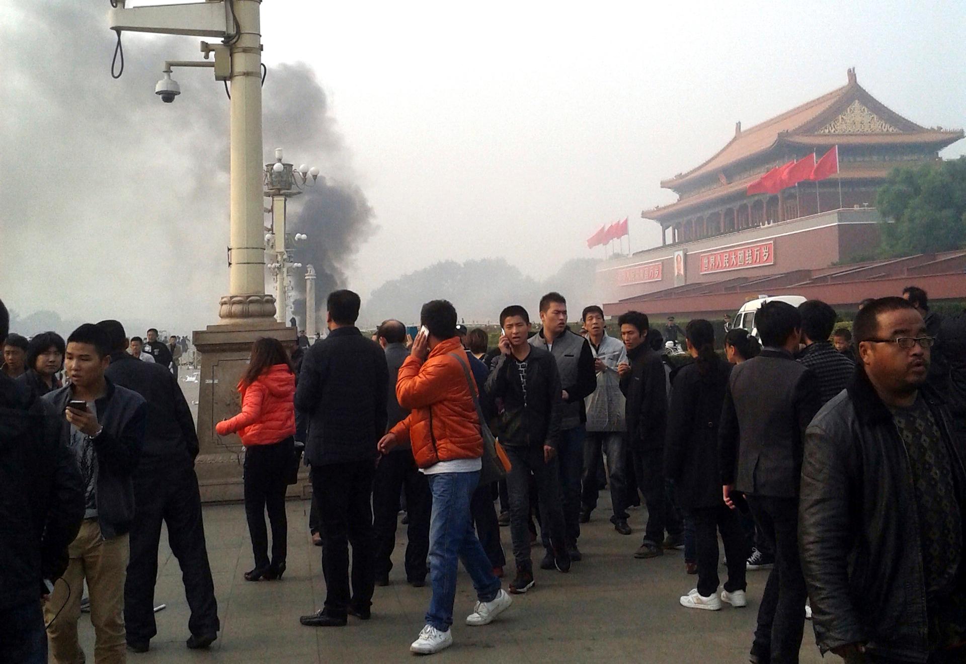 People walk along the sidewalk of Chang'an Avenue as smoke raises in front of the main entrance of the Forbidden City at Tiananmen Square in Beijing, on October 28, 2013.