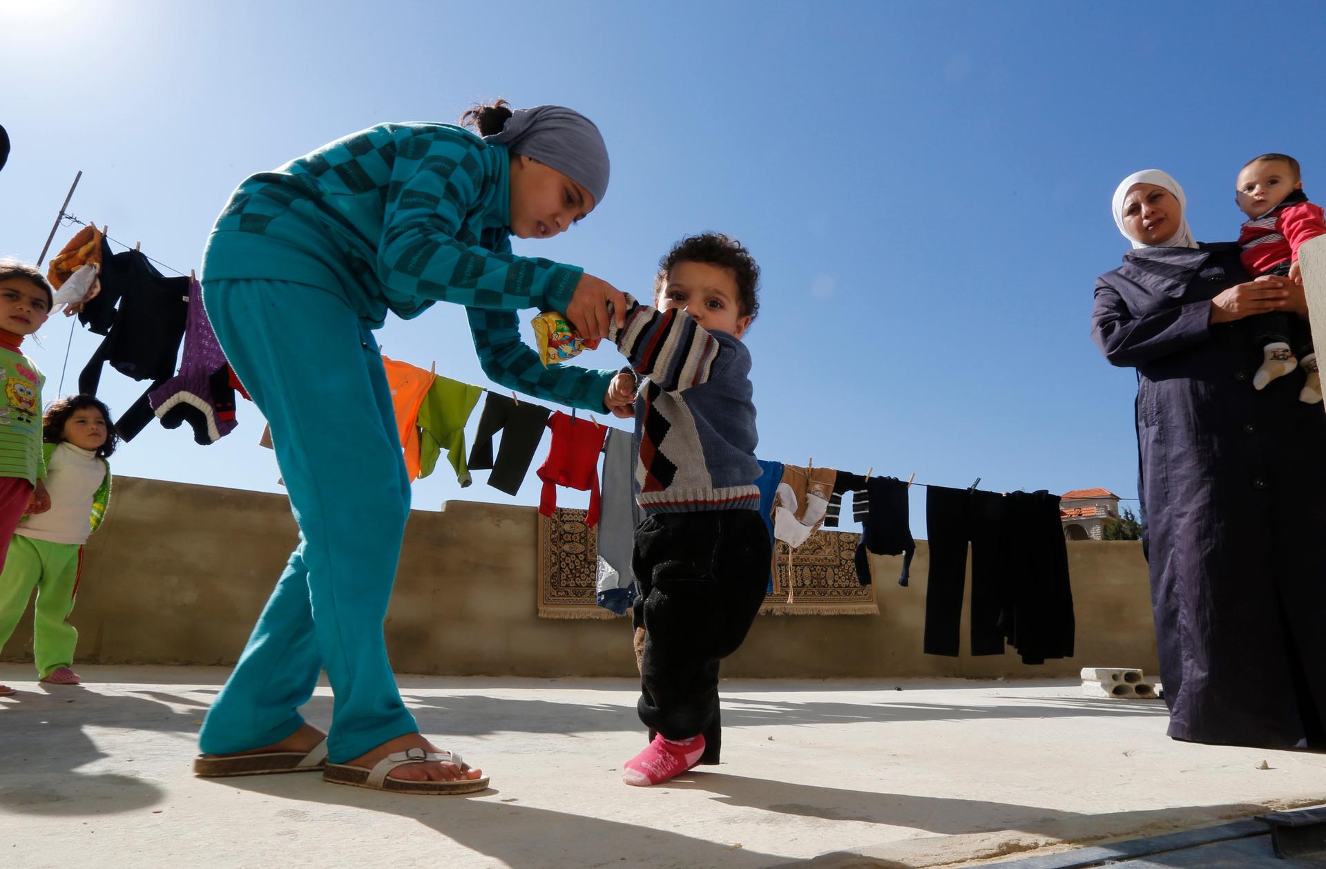 A Syrian refugee girl helps her brother walk