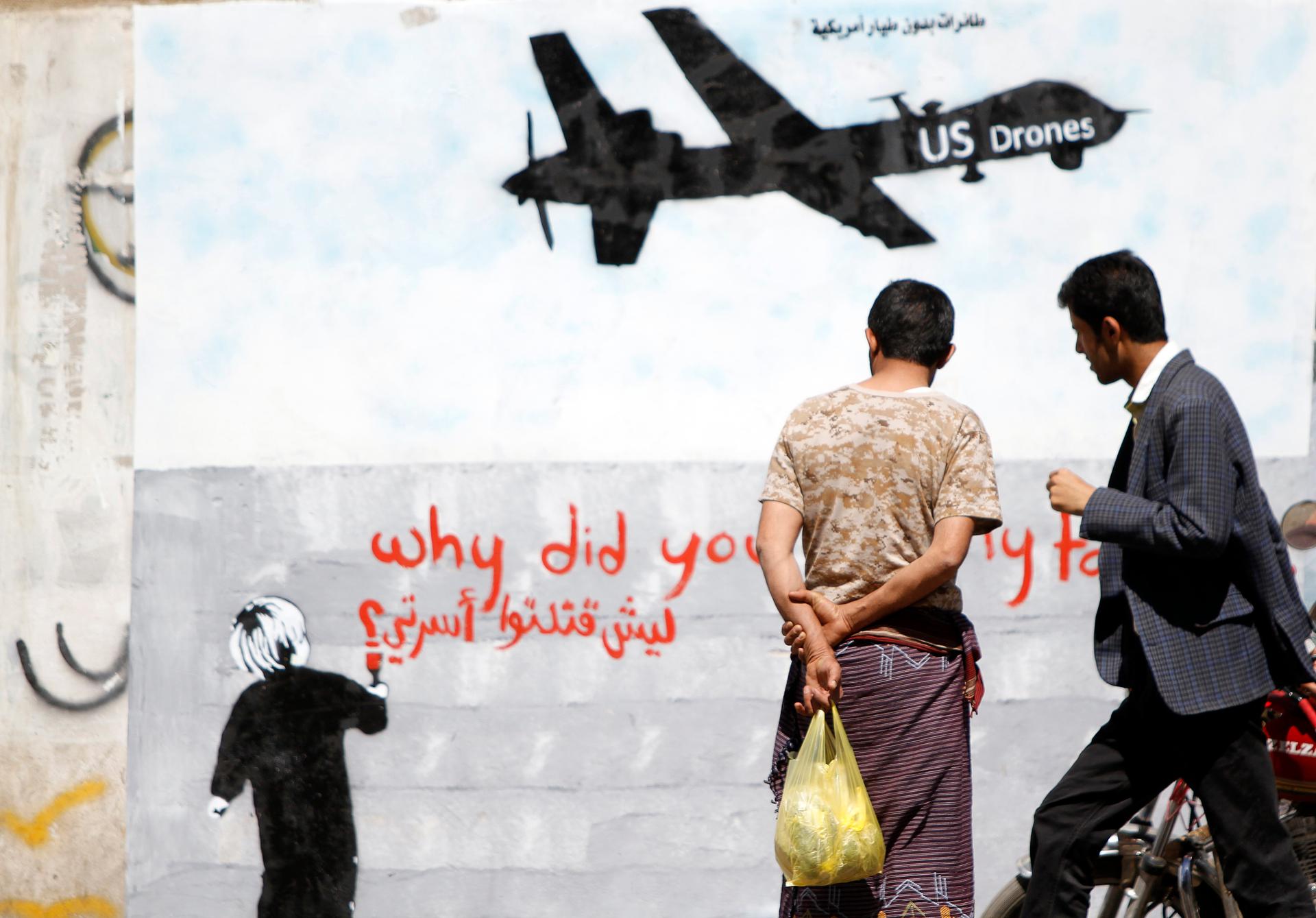 Men look at wall graffiti depicting a American drone along a street in Sana'a, Yemen, on November 9, 2013. 