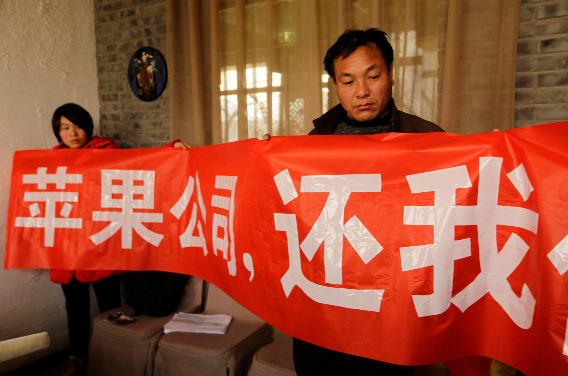 Shi Zengqiang, on the right, the father of a 15-year-old worker at Chinese manufacturing company Pegatron worker who died of pneumonia, holds a banner at a news conference in Beijing on December 16, 2013.