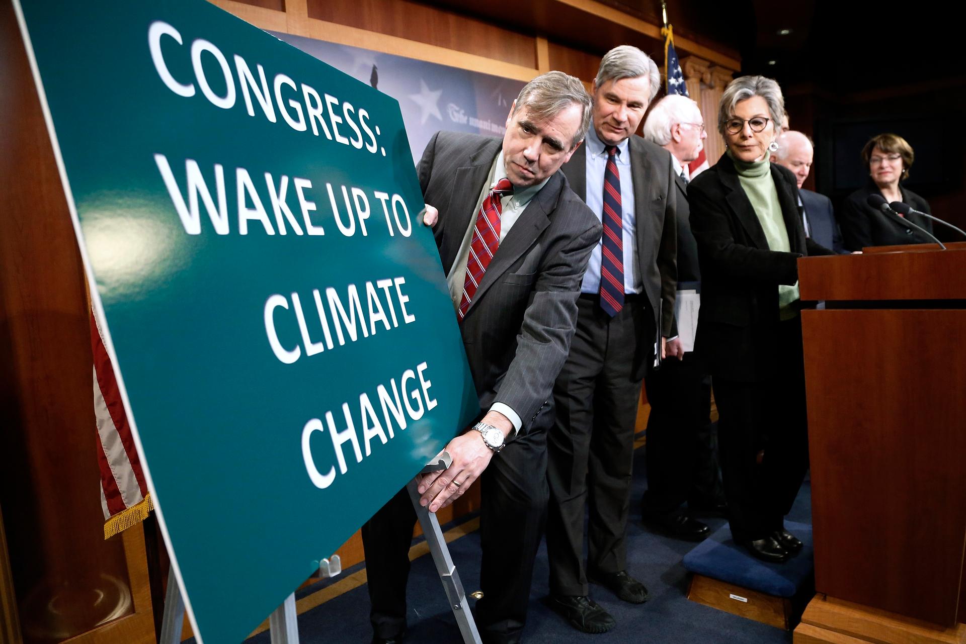 US Senator Jeff Merkley (D-Ore.) adjusts a sign at the start of a news conference led by Senator Barbara Boxer (D-Calif.) to draw attention to climate change in January 2014.