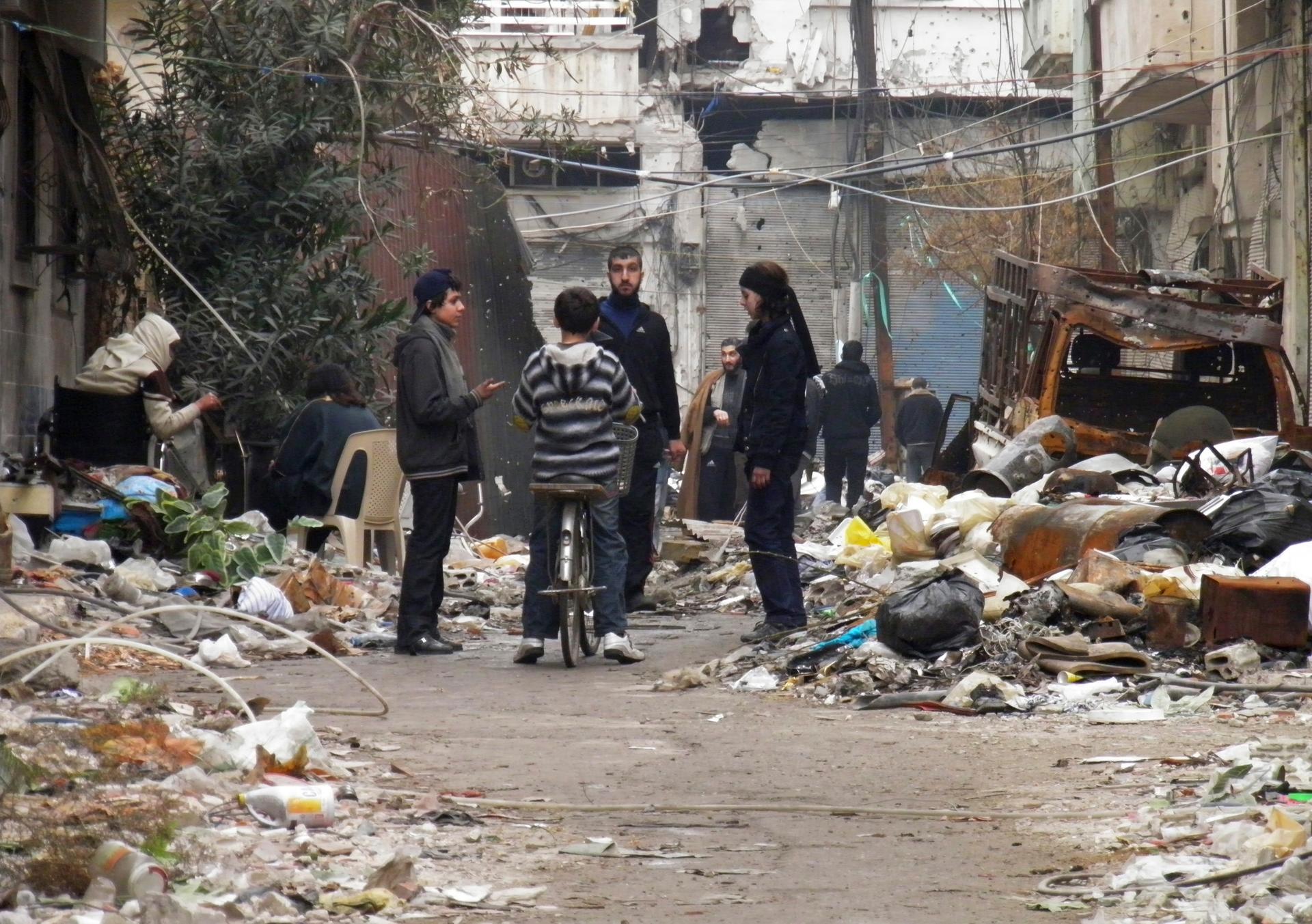 Civilians stand along a street in Homs. Washington called on the Syrian government on Monday to allow aid convoys into Homs, where "people are starving", and said that all civilians must be allowed to leave the besieged area freely.
