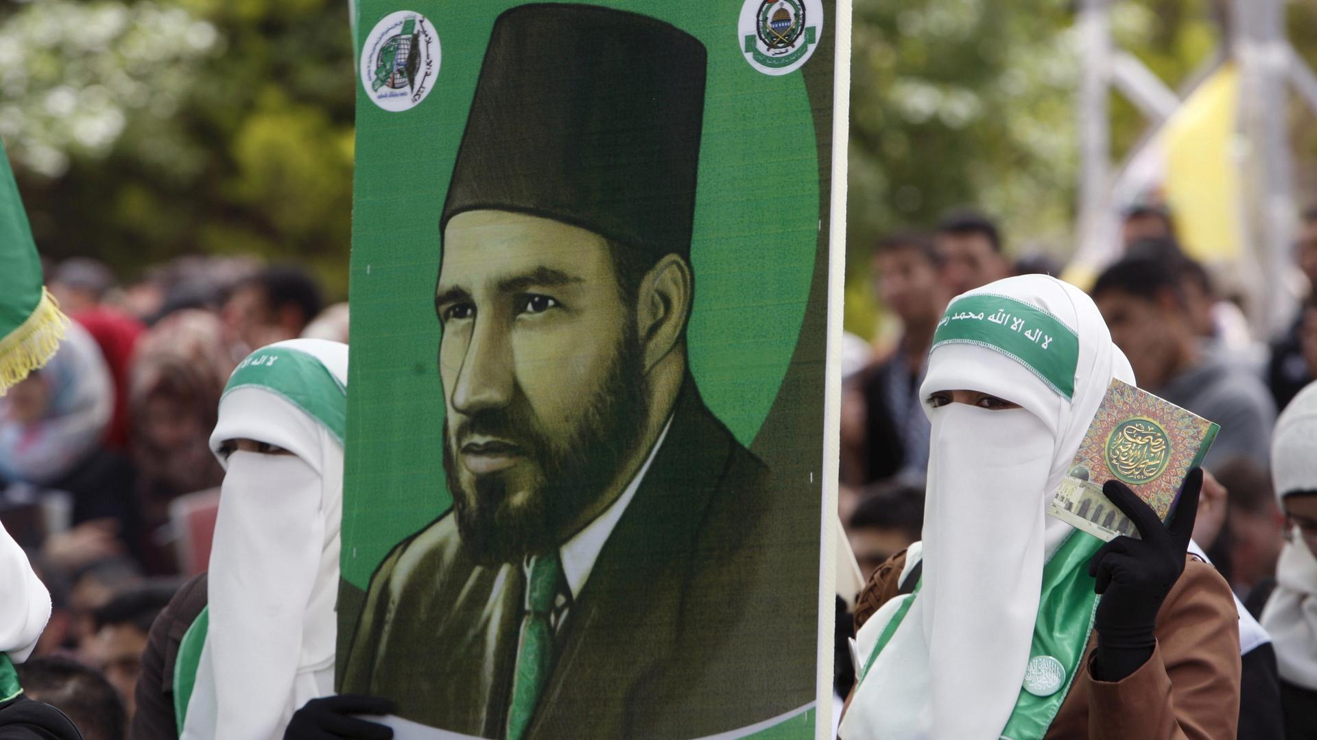 Palestinian students supporting the  militant group Hamas, an organization that's ideologically linked to the Muslim Brotherhood, hold a poster depicting Hassan Al-Banna, the Muslim Brotherhood founder, during an election campaign for students' council at