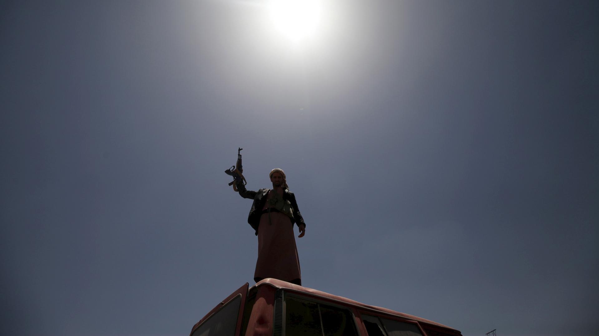 A follower of the Houthi group raises his weapon as he stands on a vehicle on a damaged street in Sanaa on April 21, 2015.