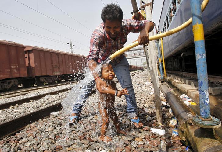 A passenger cools off a child using a pipe that supplies water to trains at a railway station on a hot summer day in the northern Indian city of Allahabad April 23, 2015. 