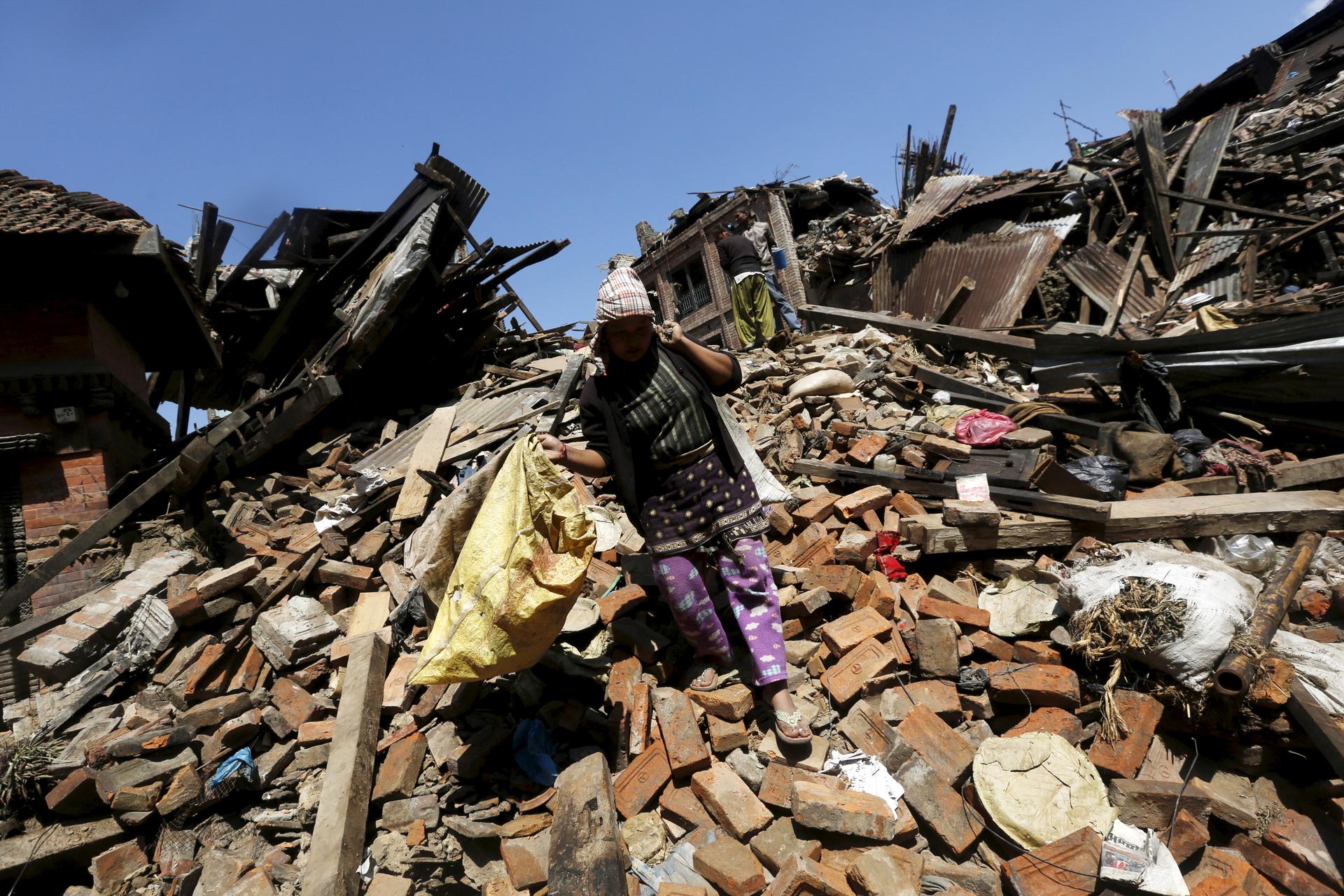A woman carries her belongings as she walks over a collapsed house in Bhaktapur, Nepal, on April 27, 2015.