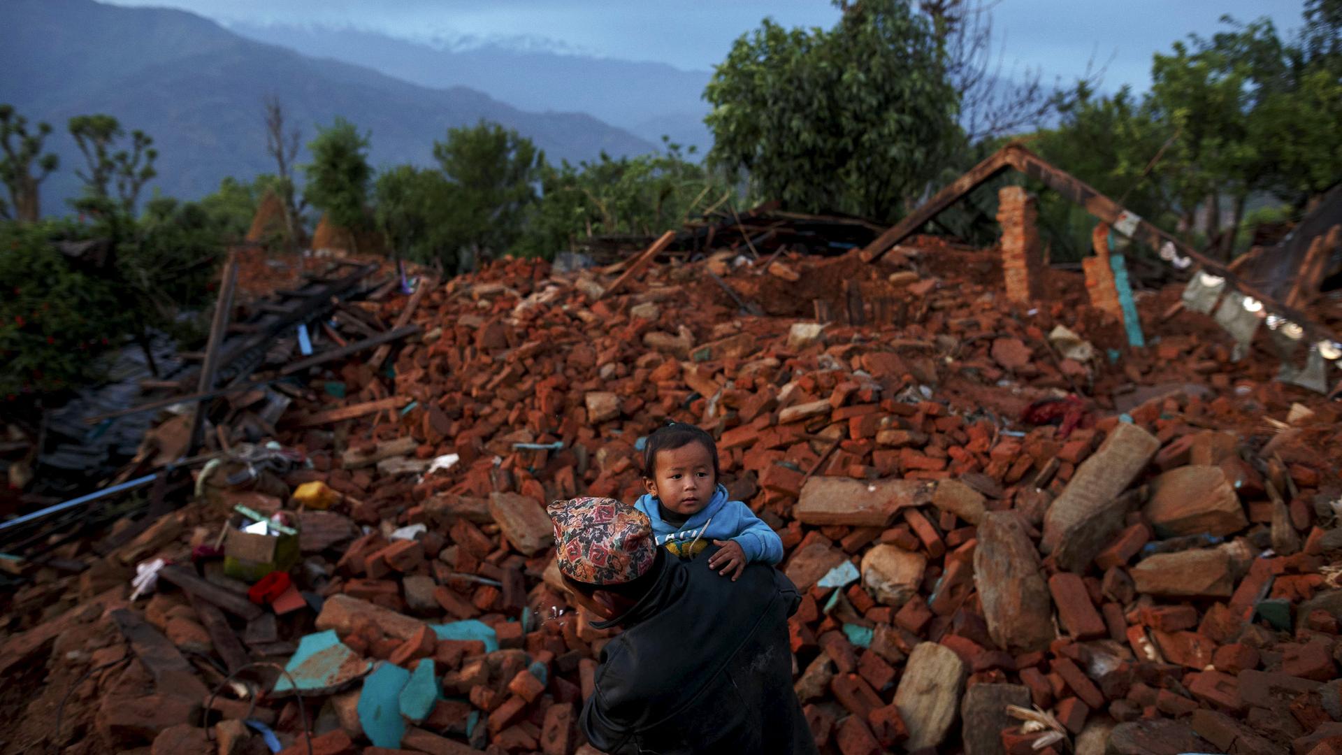 A villager carries a child amid debris in Gorkha, Nepal, following the earthquake that struck Nepal on April 25, 2015.