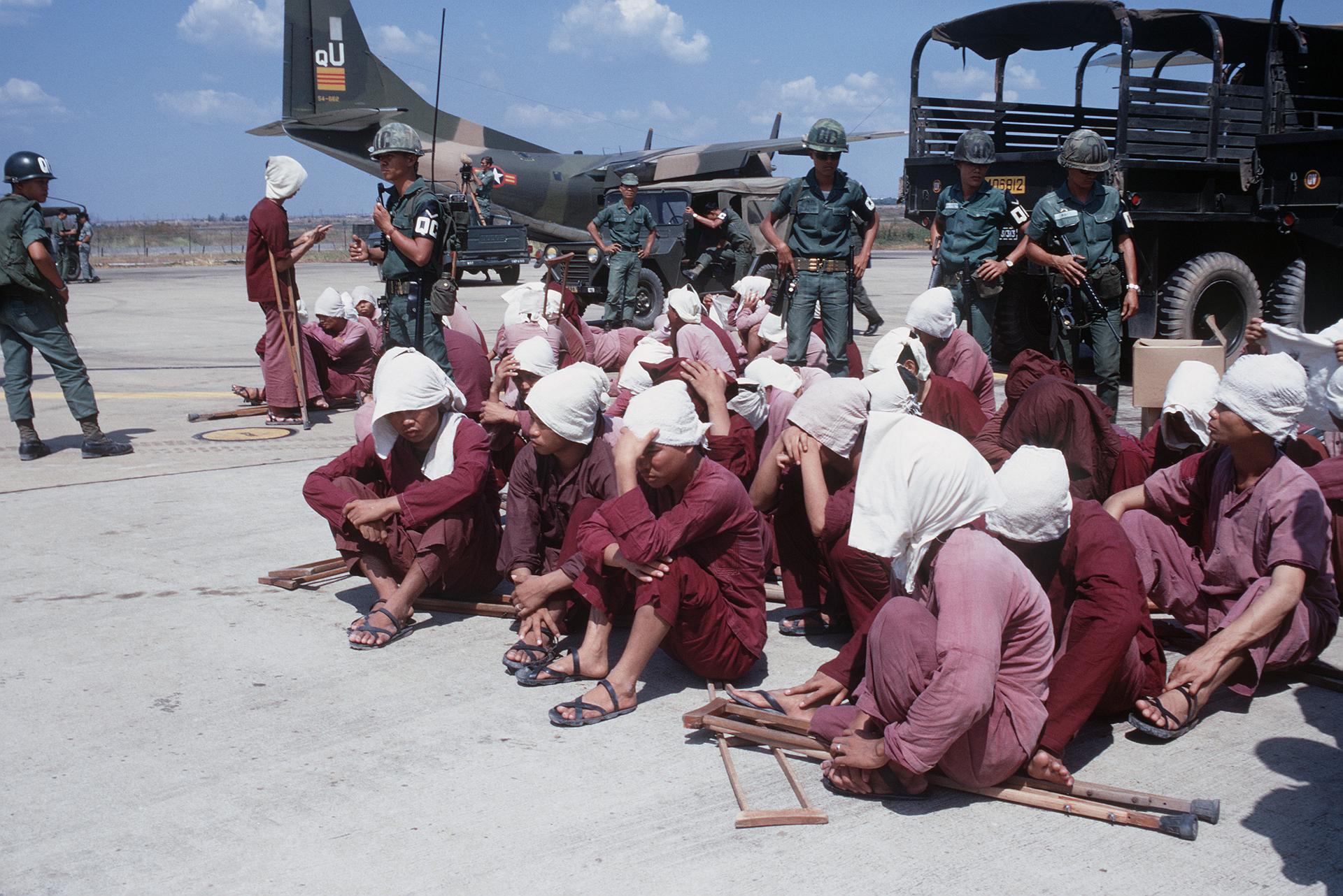 Viet Cong prisoners sit on a tarmac in Vietnam in 1973, under watch by South Vietnamese military police.