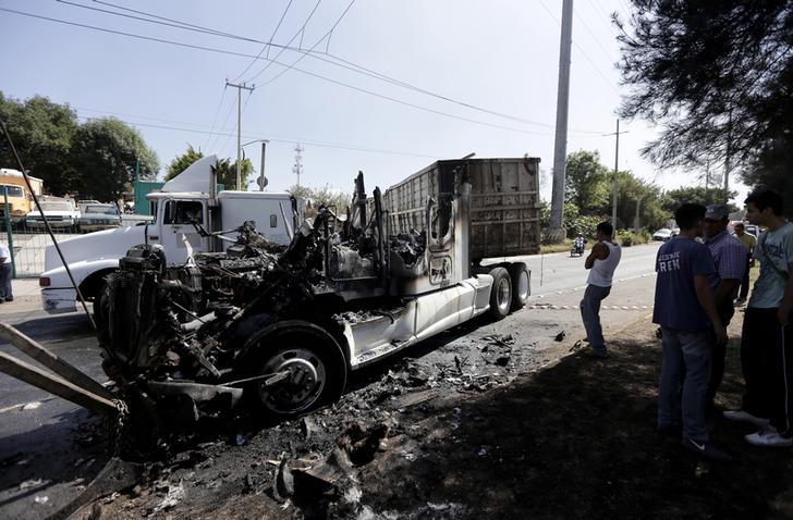 Men stand next to the wreckage of a tractor-trailer set ablaze by members of a drug cartel in Guadalajara May 1, 2015. 