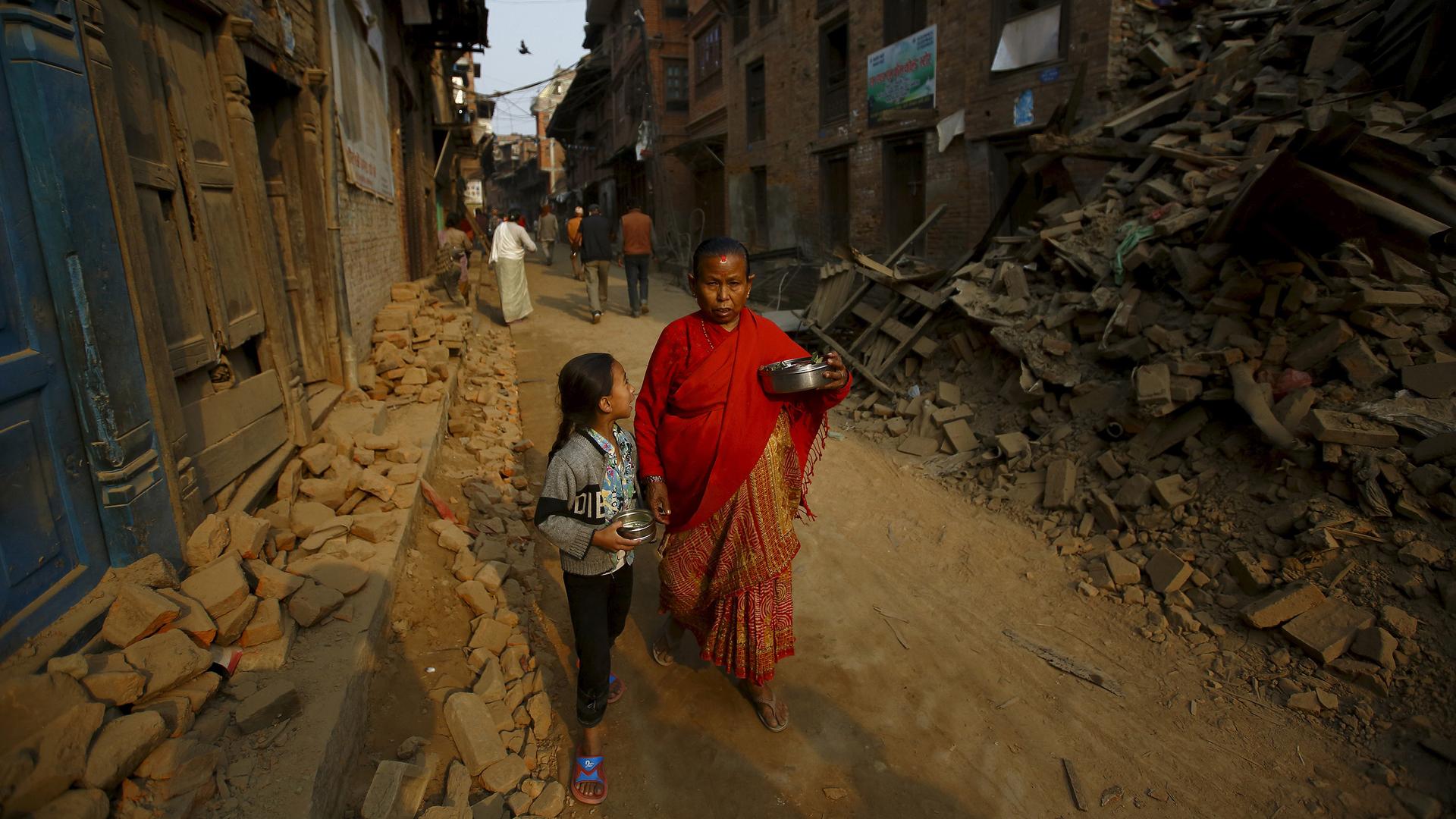 A woman and a child, returning from a temple, walk past damaged and collapsed houses following the April 25, 2015, earthquake in Nepal.