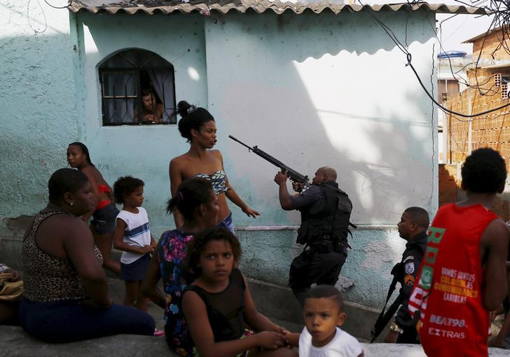 Residents observe as policemen take up position near an area where two men were found dead on top of the Sao Carlos slums complex in Rio de Janeiro May 15, 2015.