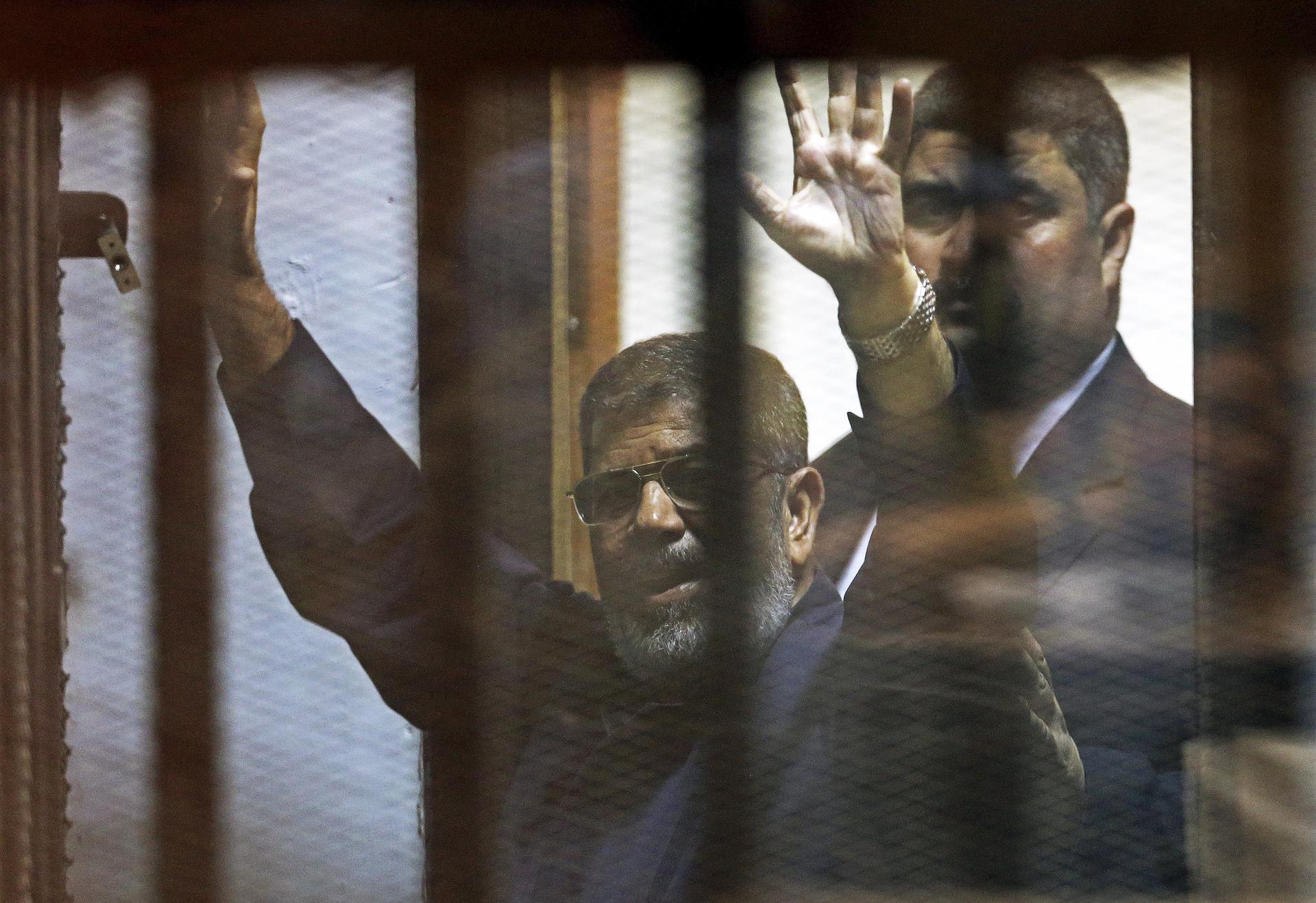 Deposed Egyptian President Mohamed Morsi greets his lawyers and people from behind bars after his verdict at a court on the outskirts of Cairo, Egypt on June 16, 2015.