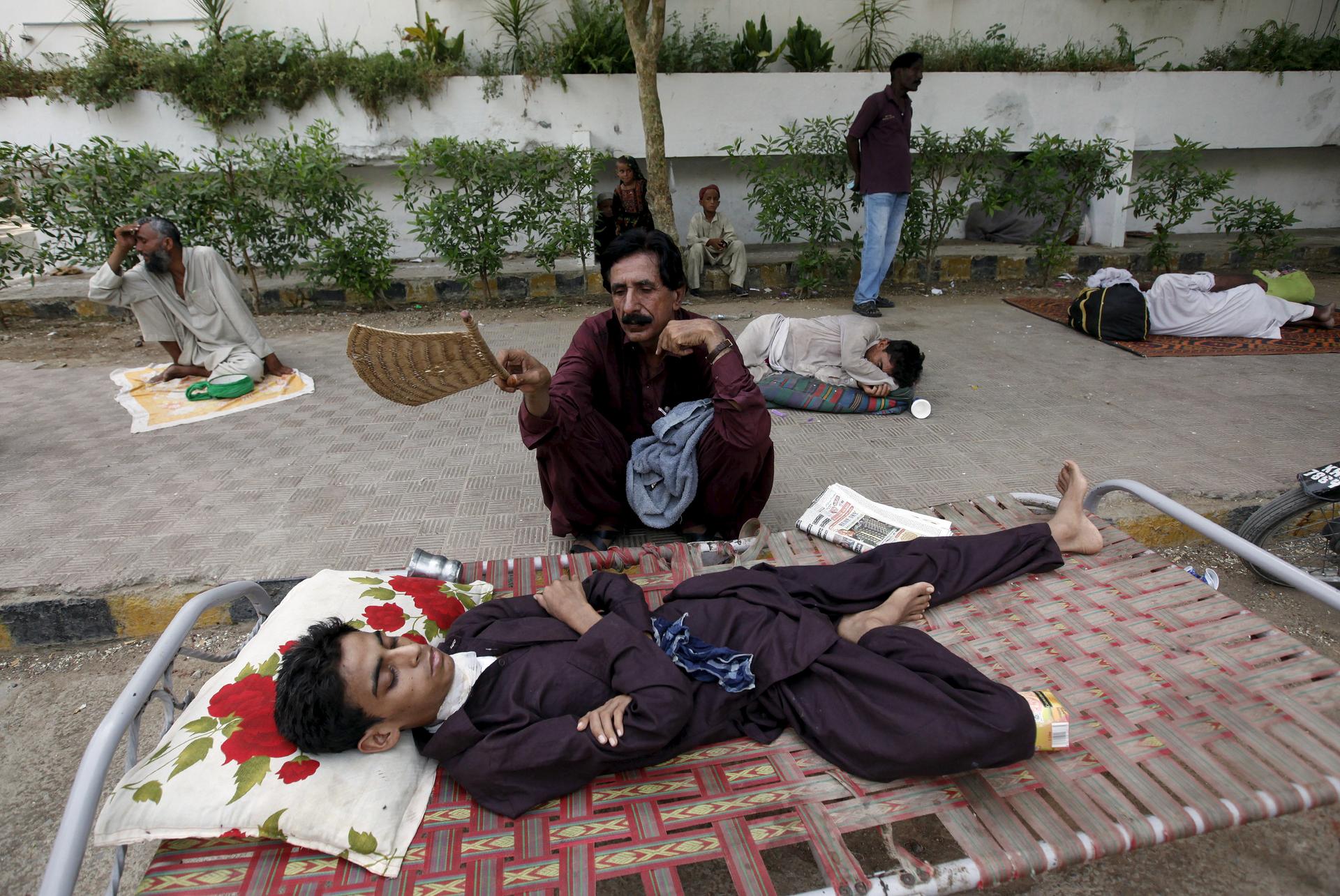A man uses a hand-held fan to cool down his son, while waiting for their turn for a medical checkup, outside Jinnah Postgraduate Medical Centre (JPMC) during intense hot weather in Karachi, Pakistan, June 23, 2015.