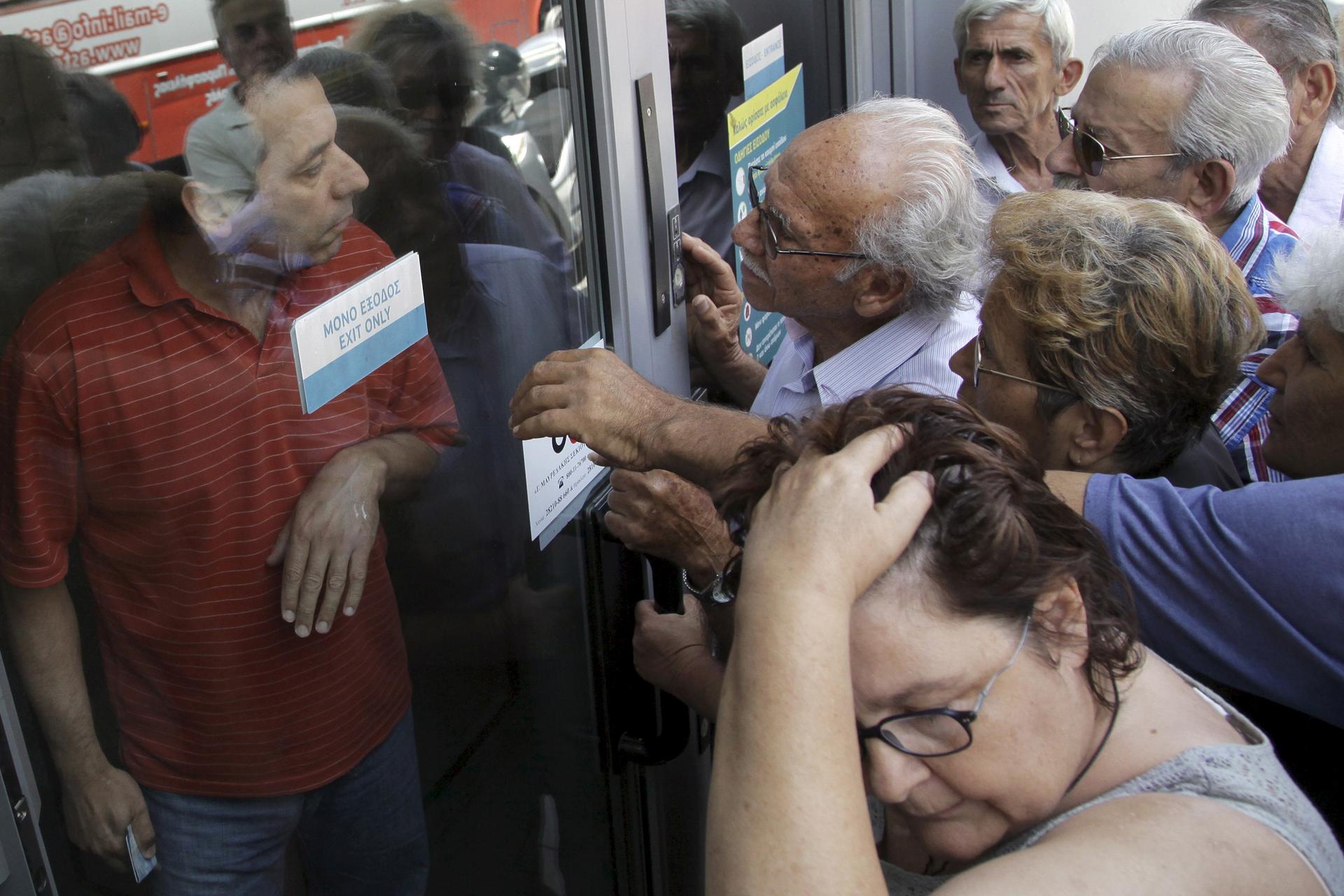 Pensioners waiting outside a closed National Bank branch and hoping to get their pensions, argue with a bank employee (L) in Iraklio on the island of Crete, Greece June 29, 2015. Greeks struggled to adjust to shuttered banks, closed cash machines and a cl