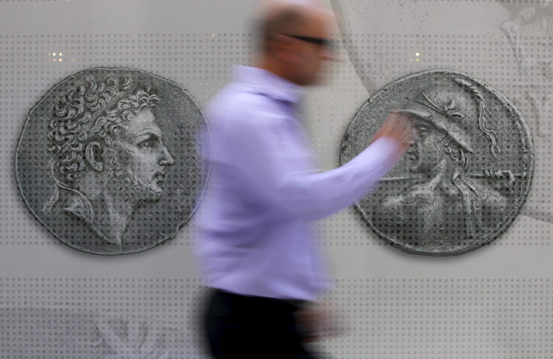 A man walks past pictures of ancient coins in central Athens