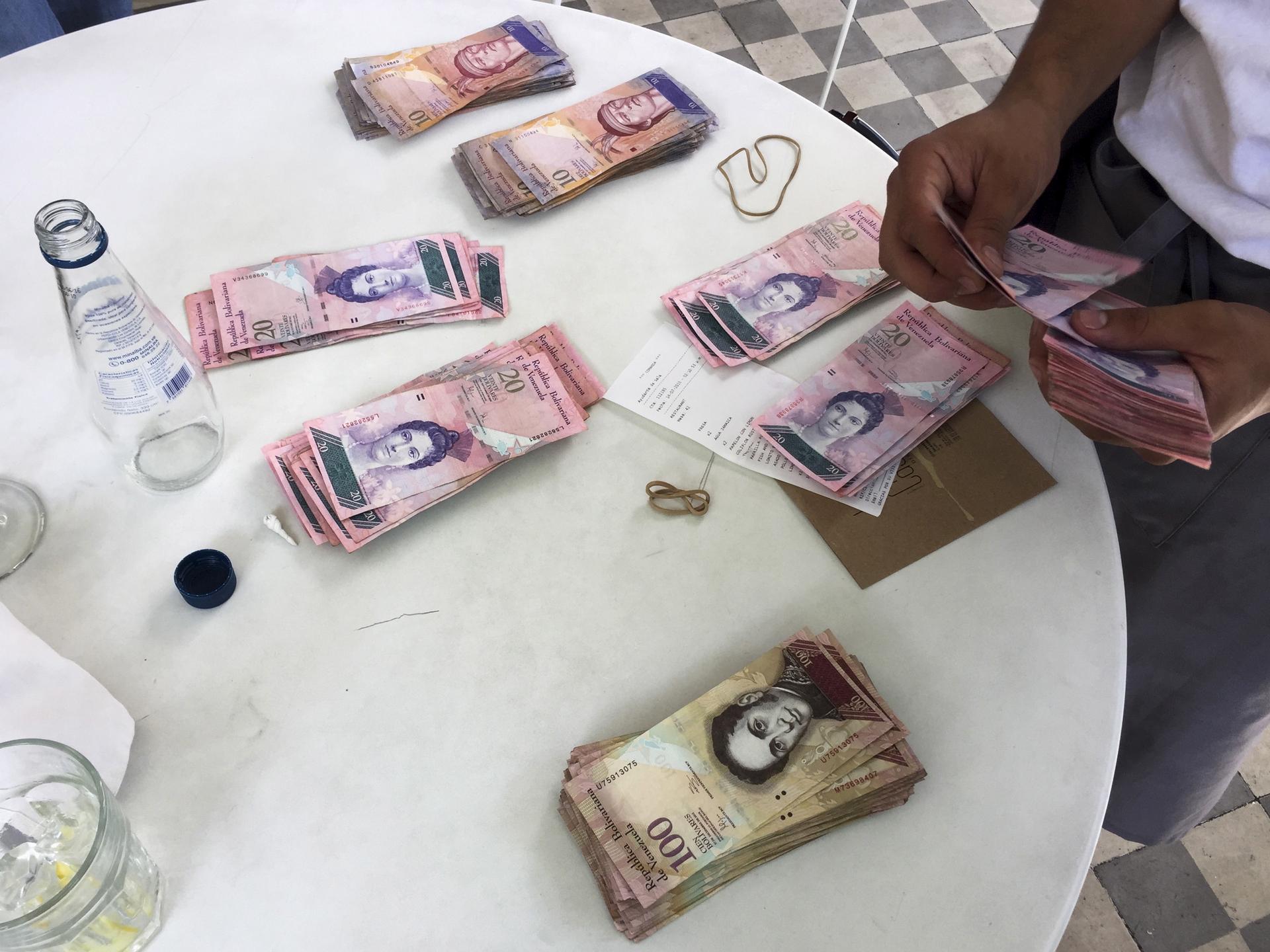 A waiter counts Venezuelan bolivar notes, corresponding to the bill for a lunch of 4 people.