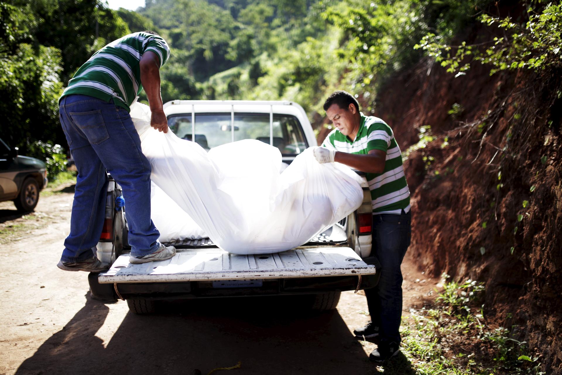Two workers holding a white body body bag as they place it in the back of a truck