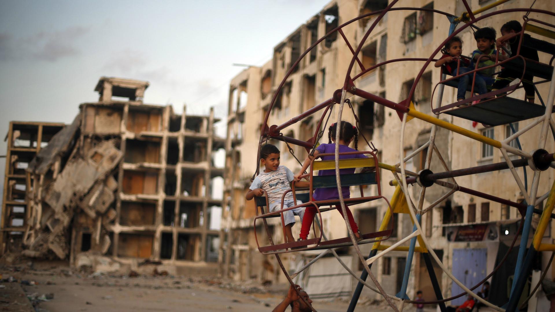 Palestinian children play on a ferris wheel near residential buildings that witnesses said were destroyed by Israeli shelling during a 50-day war in the summer of 2014, in Beit Lahiya town in the northern Gaza, July 27, 2015.