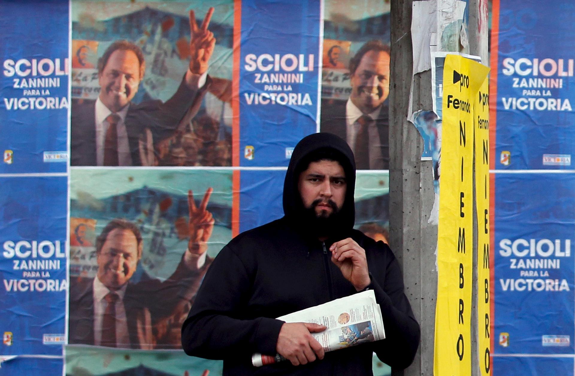 A man stands at a bus stop in front of campaign posters advertising Buenos Aires' province governor and presidential candidate Daniel Scioli, ahead of August 9 party primary elections