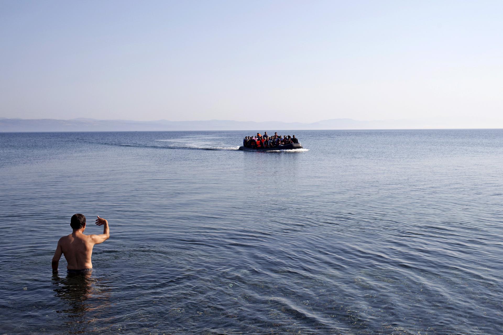 A local man gestures to Syrian refugees on a dinghy approaching the shores of the Greek island of Lesbos, September 4, 2015. 