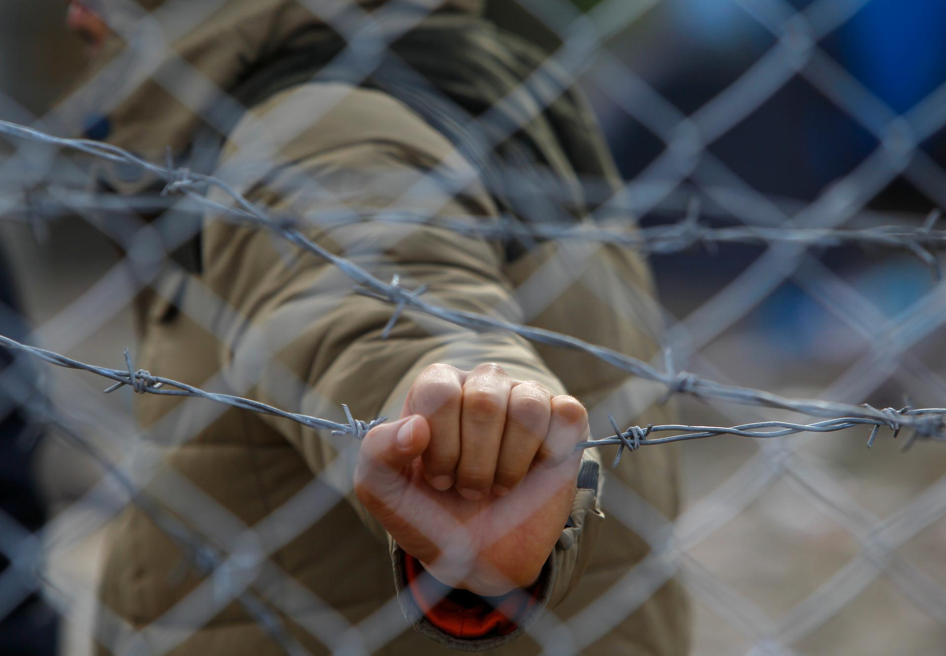 A migrant holds a barbed wire fence at the Macedonian-Greek border, near Gevgelija, Macedonia, November 29, 2015.