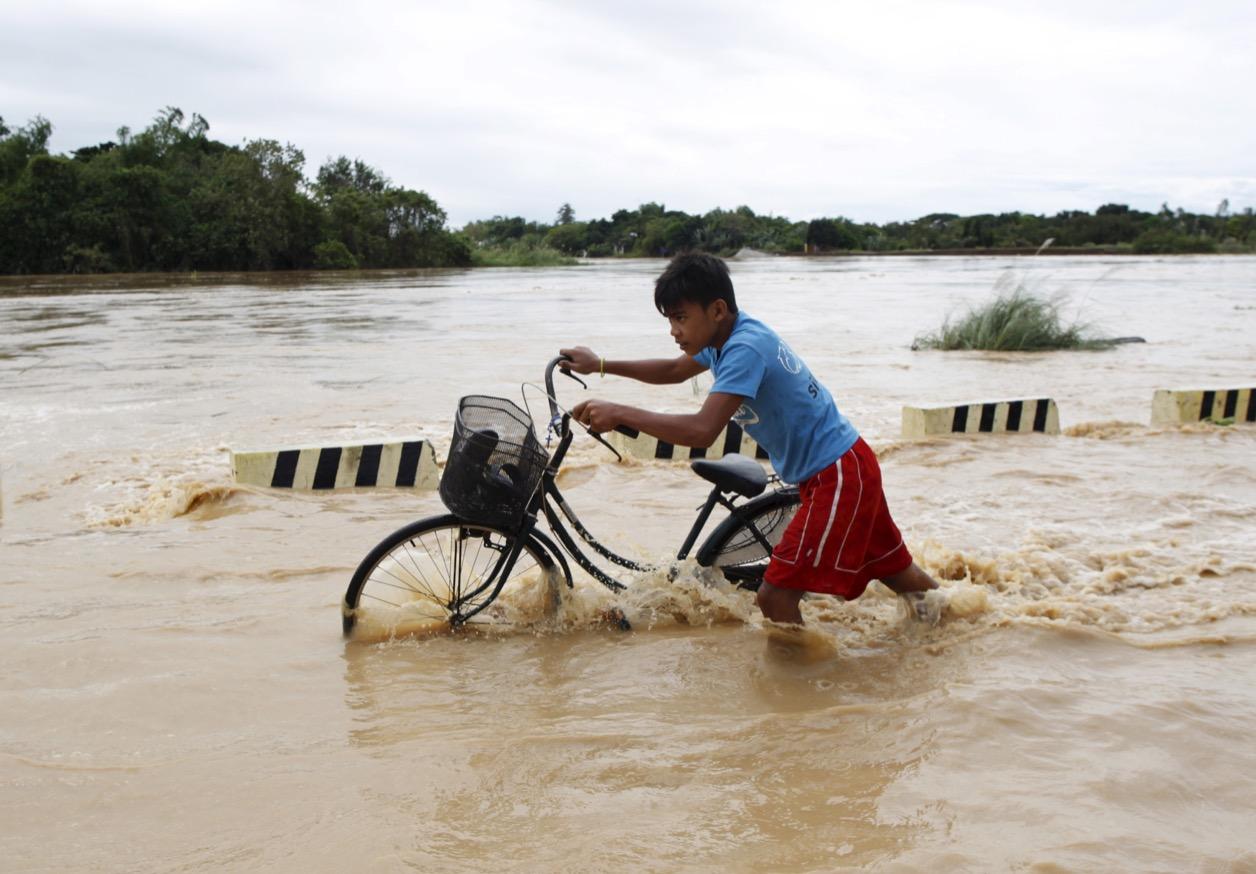 A boy pushes his bike through a flooded road after heavy rain in Candaba, Pampanga province, Philippines on Dec. 17, 2015.