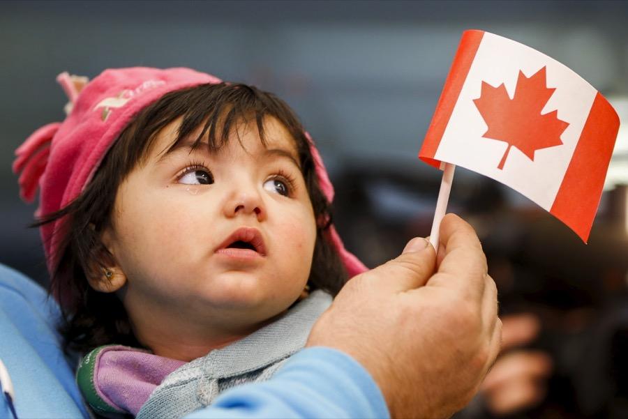 A young Syrian refugee looks up as her father holds her and a Canadian flag at the as they arrive at Pearson Toronto International Airport in Mississauga, Ontario, Dec. 18, 2015.