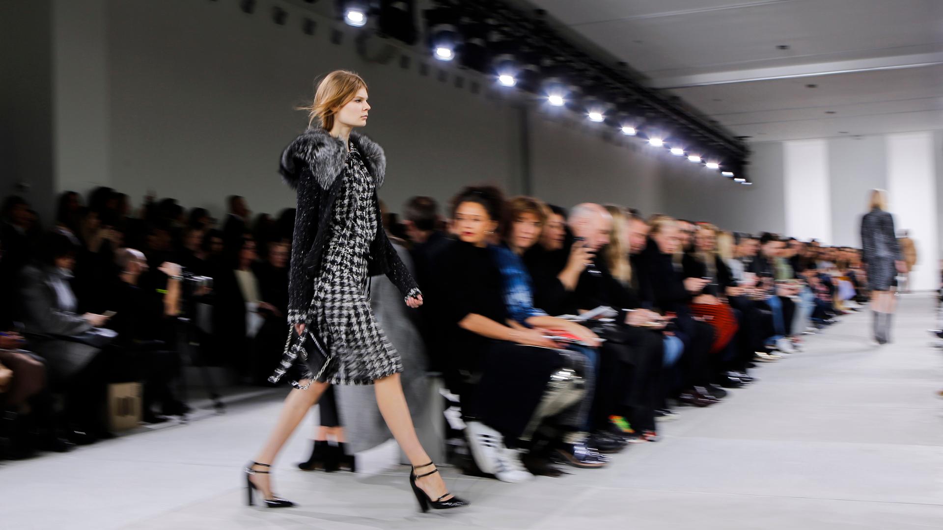 A woman walks on a catwalk around people sitting in chairs