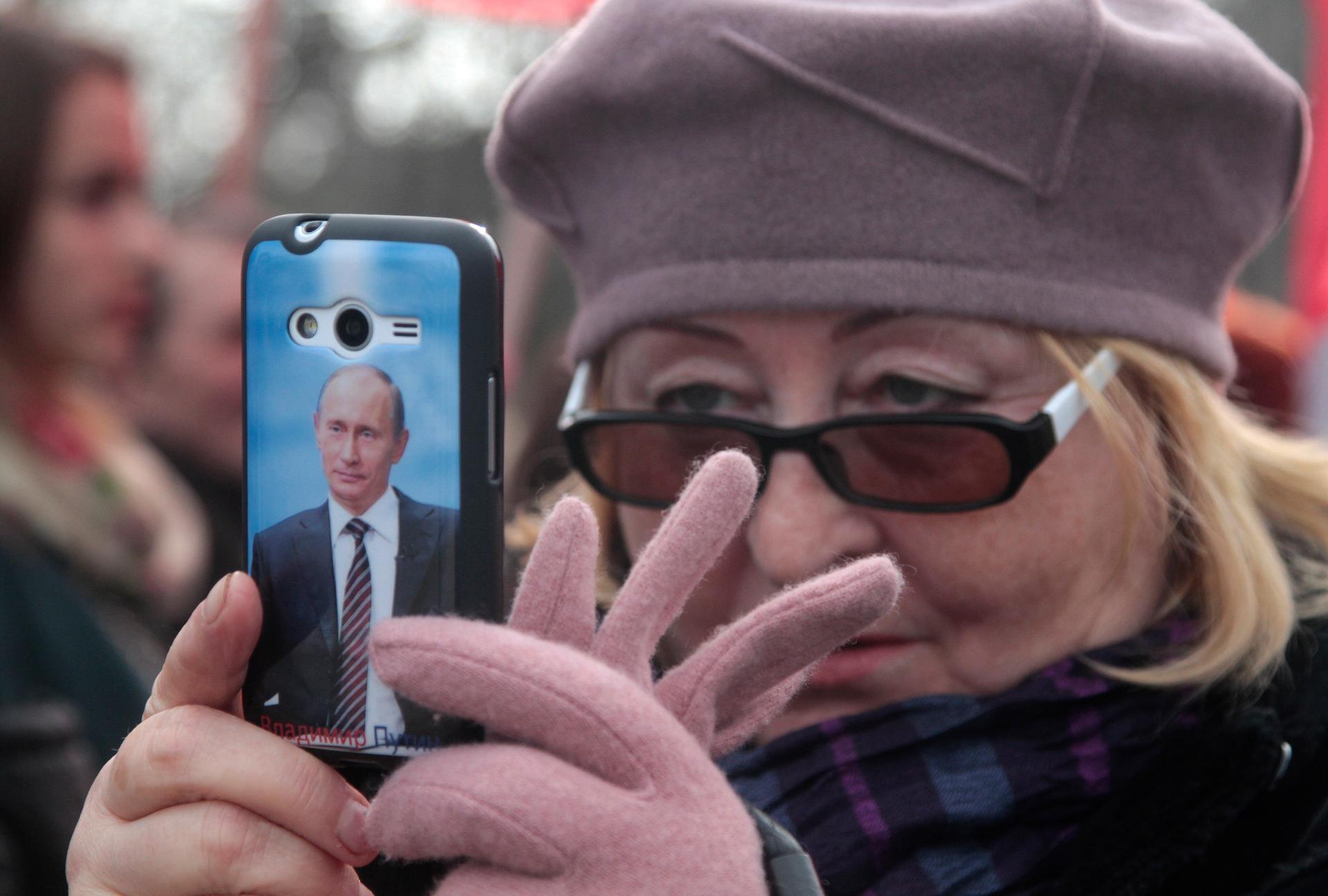 A woman holds a phone with a picture of Vladimir Putin on it.