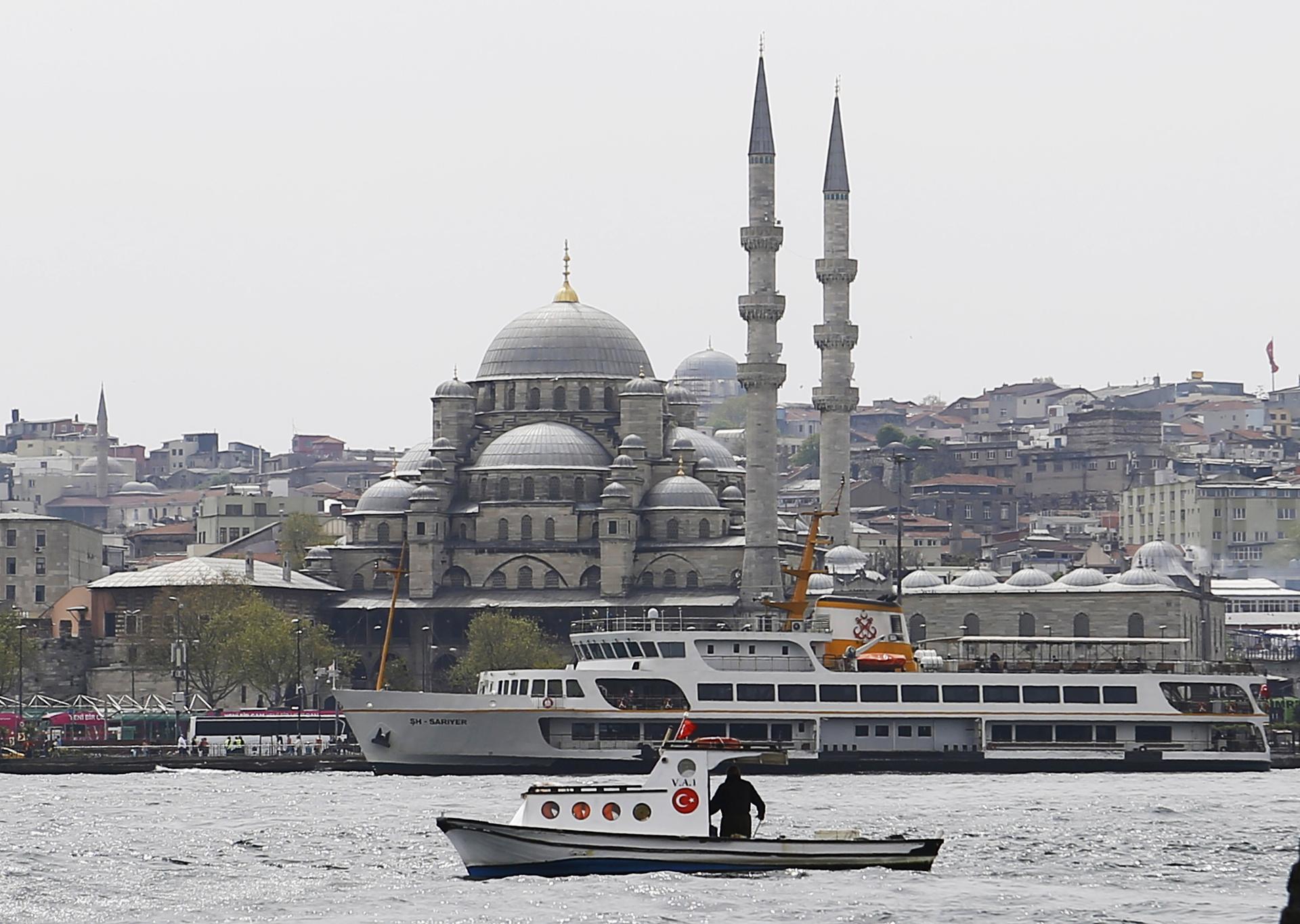 A fishing boat sails in the Golden Horn with the 17th-century Yeni Cami mosque in the background in Istanbul, Turkey.