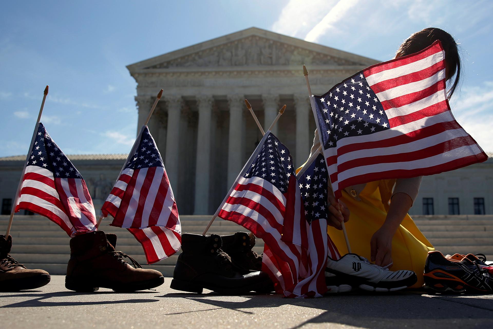 A woman puts flags in a line of shoes on a sunny day in front of Supreme Court building