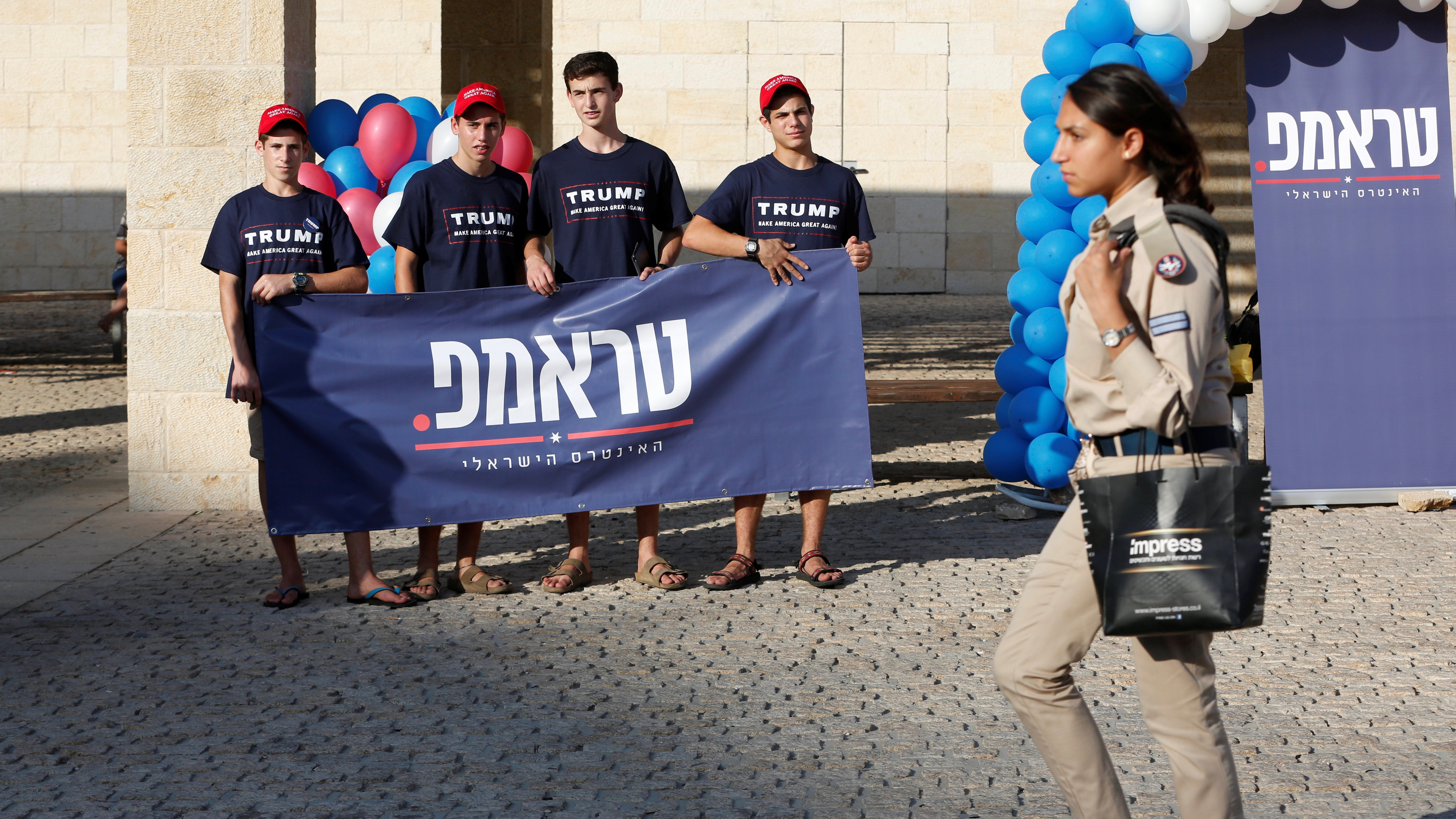 An Israeli soldier walks past U.S. Republican Party activists in Israel, who are holding a banner in support of their presidential nominee, Donald Trump, during a campaign aimed at potential American voters living in Israel, near a mall in Modi'in, Israel
