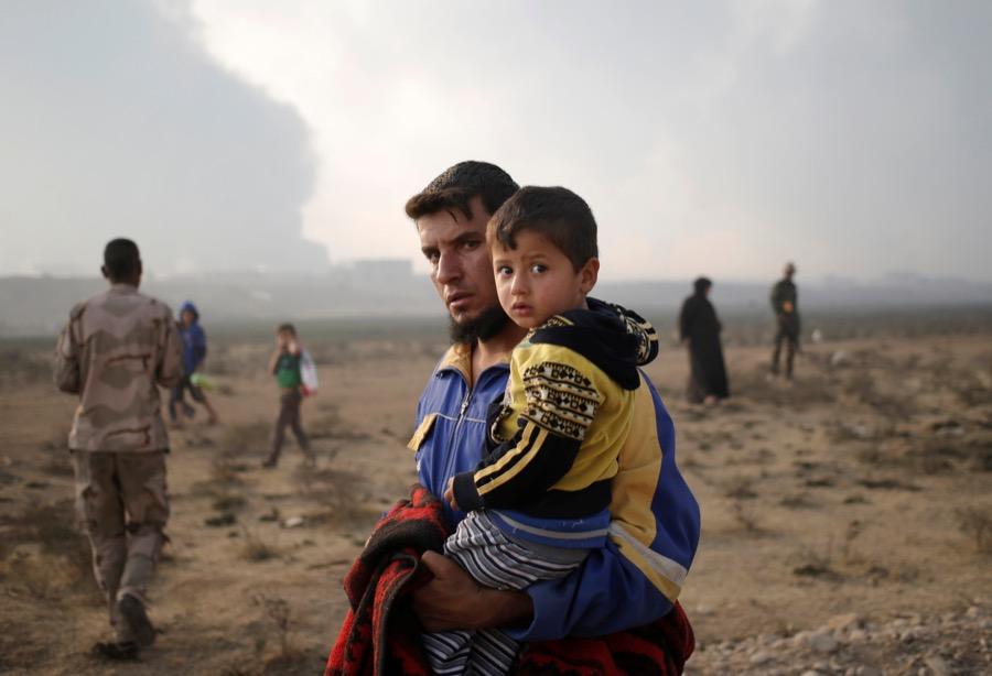 A newly displaced man carries a boy at a check point in Qayyara, east of Mosul, Iraq on Oct. 26.
