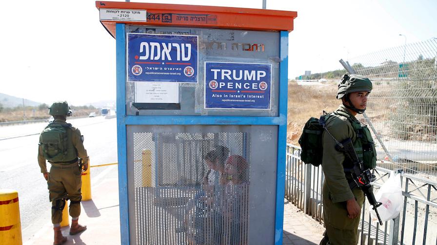 Israeli soldiers at a bus stop covered with posters from the Israeli branch of the US Republican Party, near the West Bank Jewish settlement of Ariel on Oct. 6.