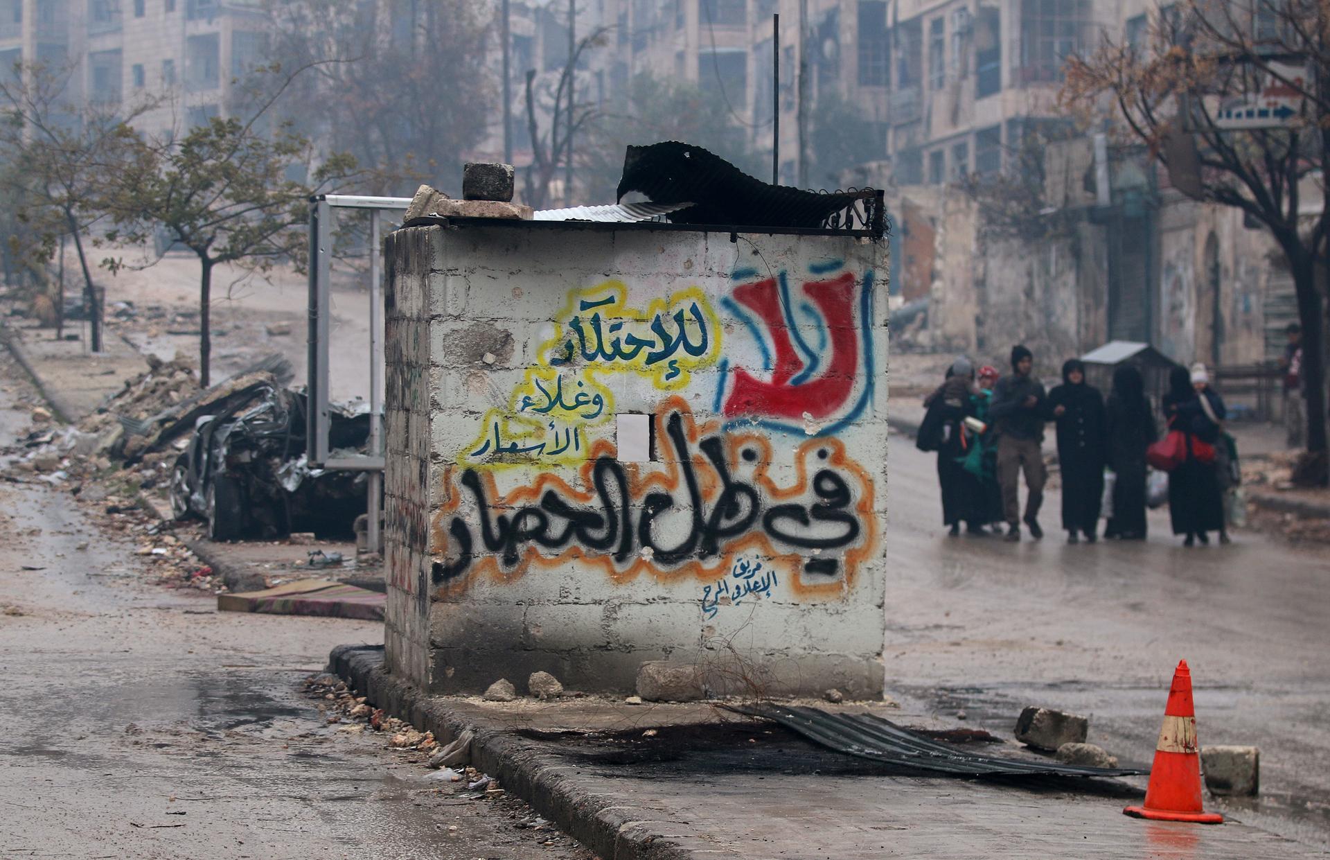 People carry their belongings as they flee deeper into the remaining rebel-held areas of Aleppo, Syria December 13, 2016. The Arabic words read, "No to monopolizing commodities and raising prices under the siege."