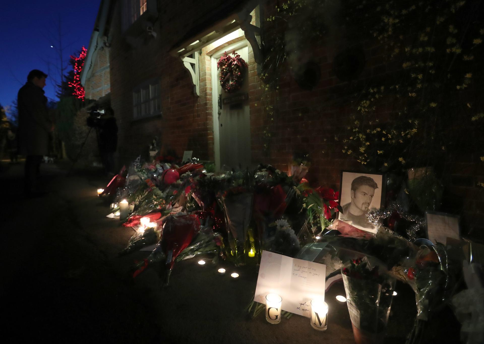 Flowers, cards and portrait of George Michael in front of brick building